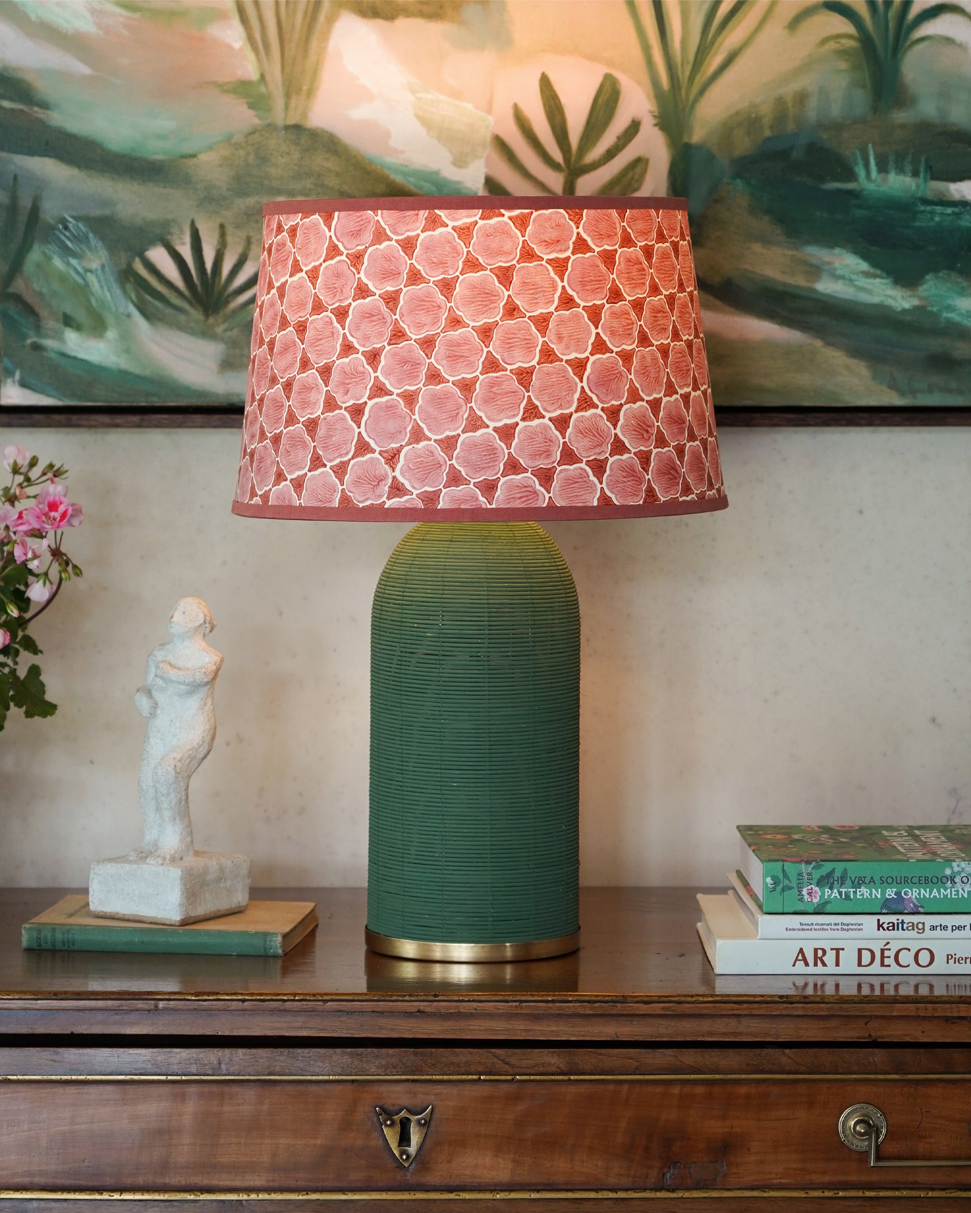 Table lamp with pink textured shade and green rattan lamp base on a wooden surface with decorative items.