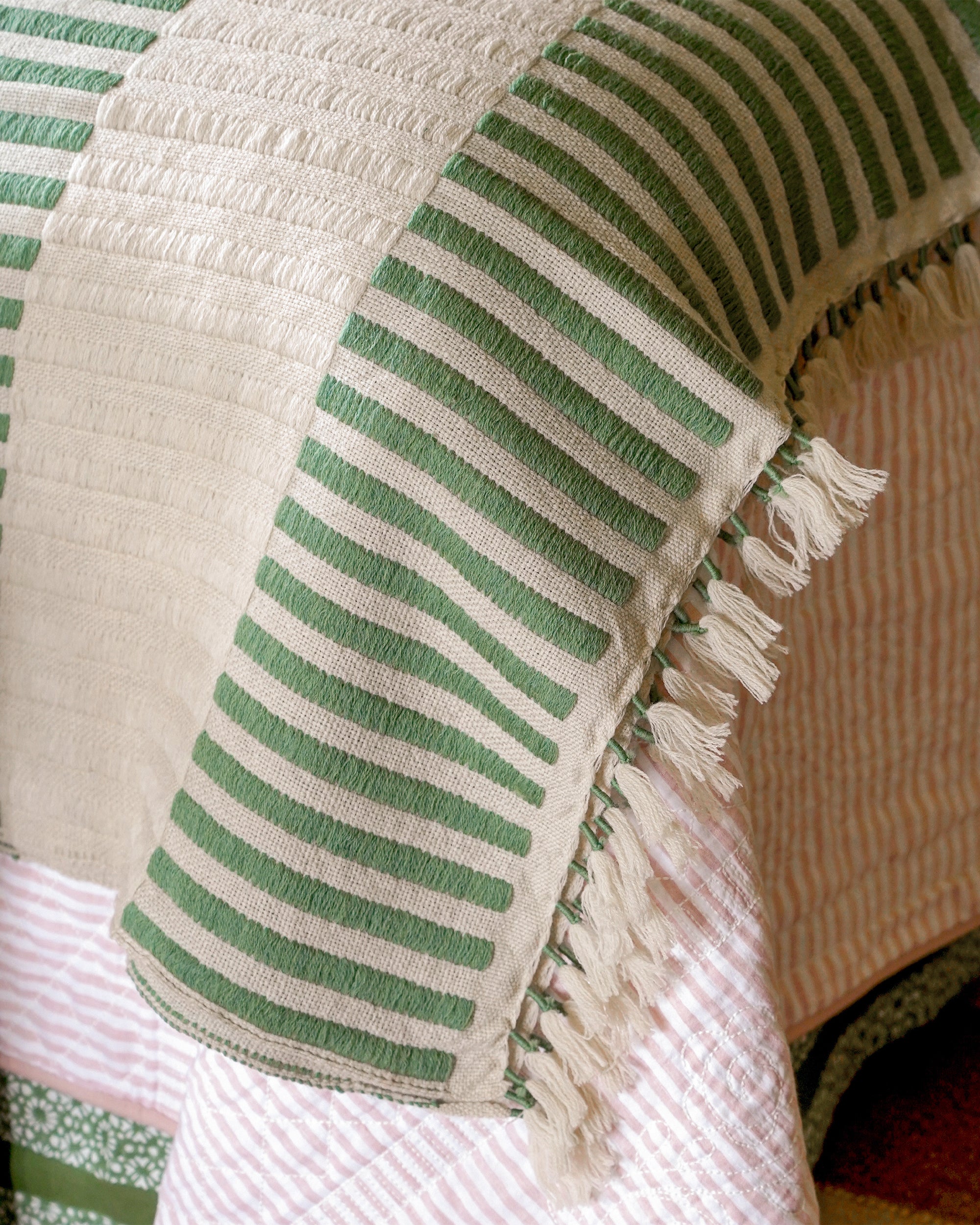 Close-up of a green and white striped throw with tassels on a textured surface.