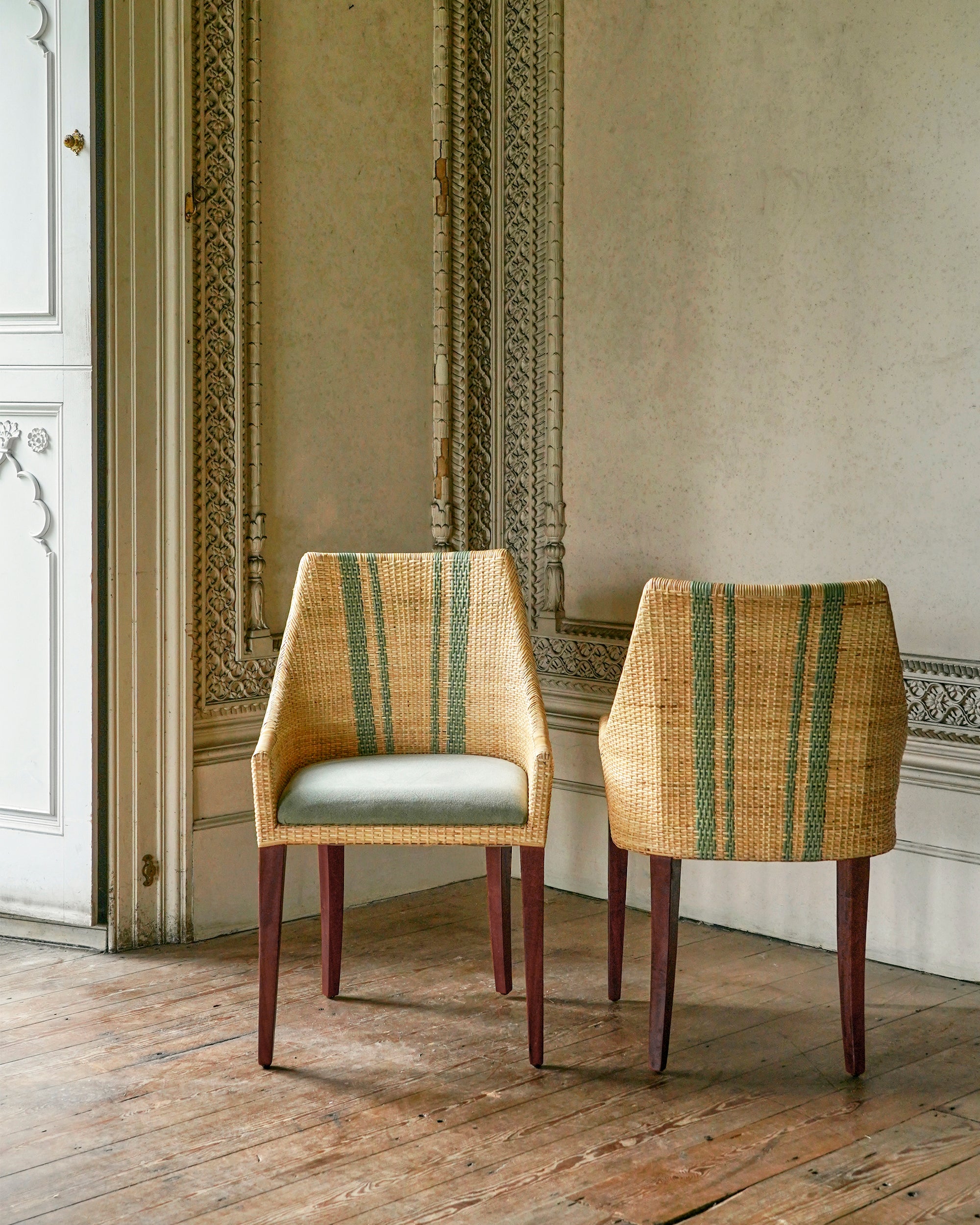 Two rattan dining chairs with striped backs in a room with ornate wall decorations.