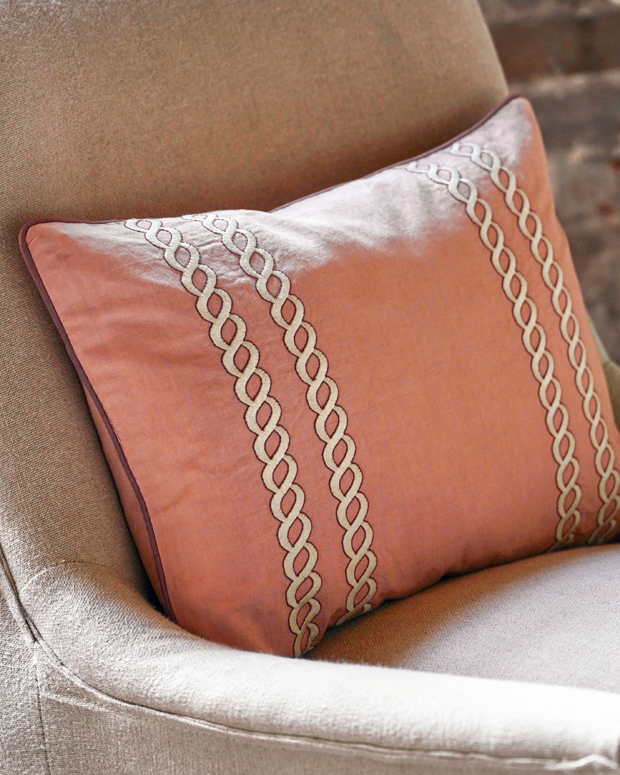 Decorative pink cushion with chain pattern on a beige sofa