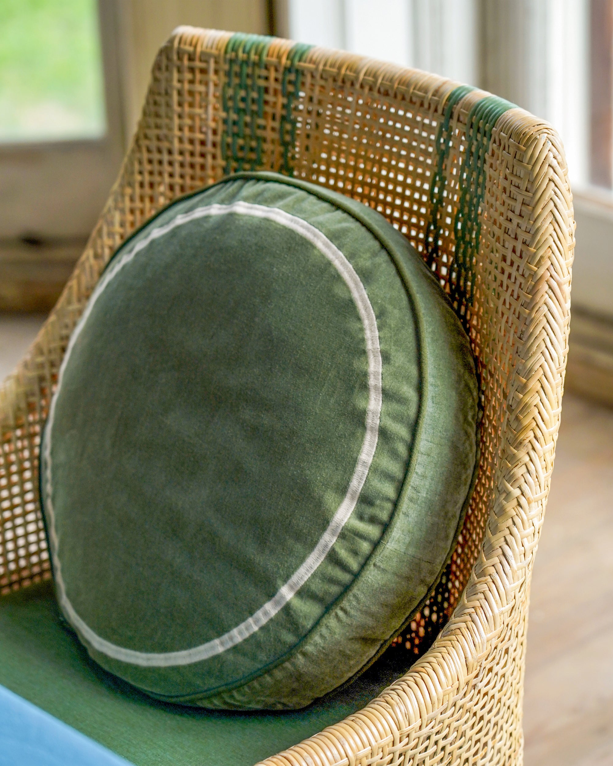 Green round cushion on a wicker chair with a blurred indoor background