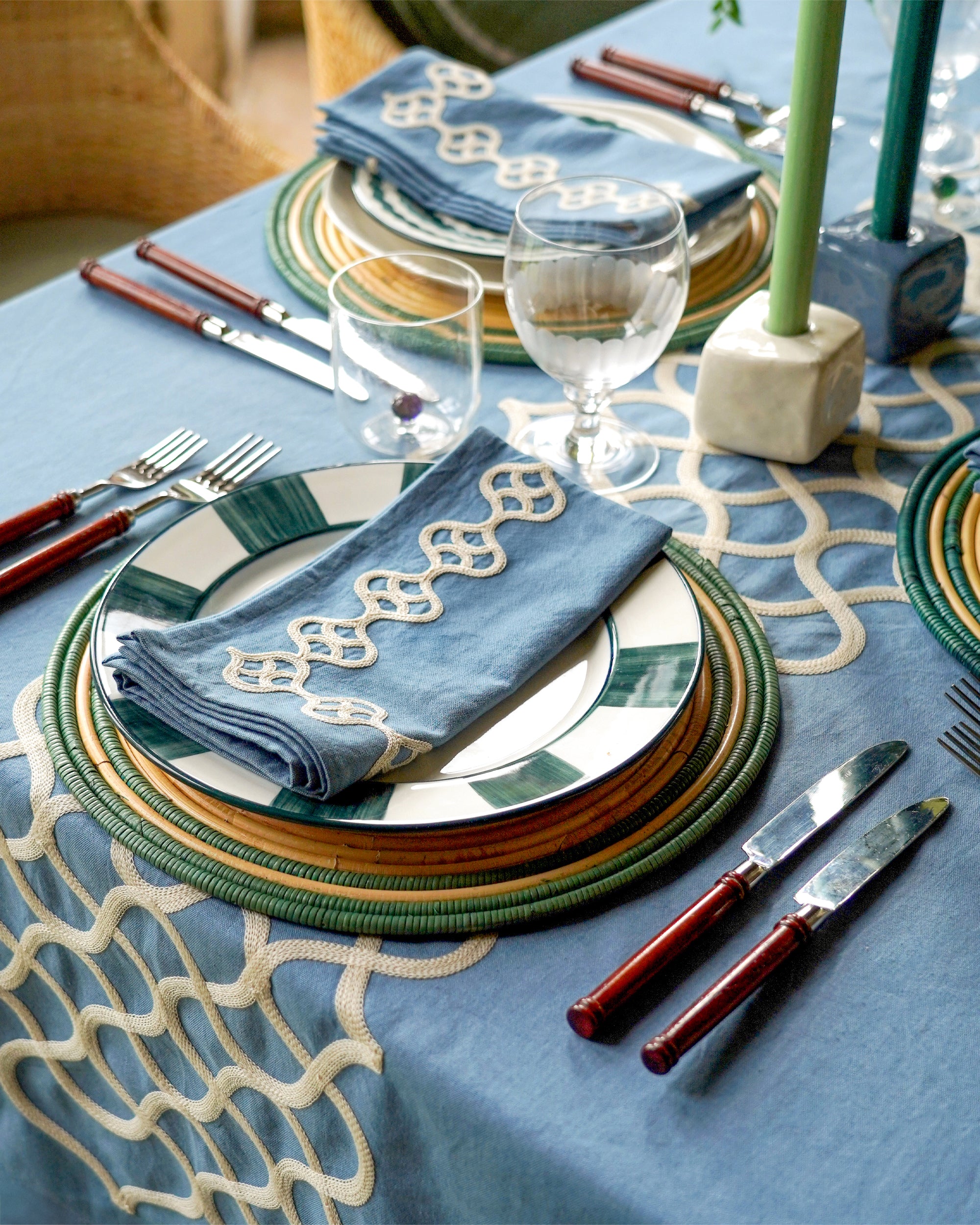 Elegant table setting with decorative plates, napkins, and cutlery on a blue tablecloth.