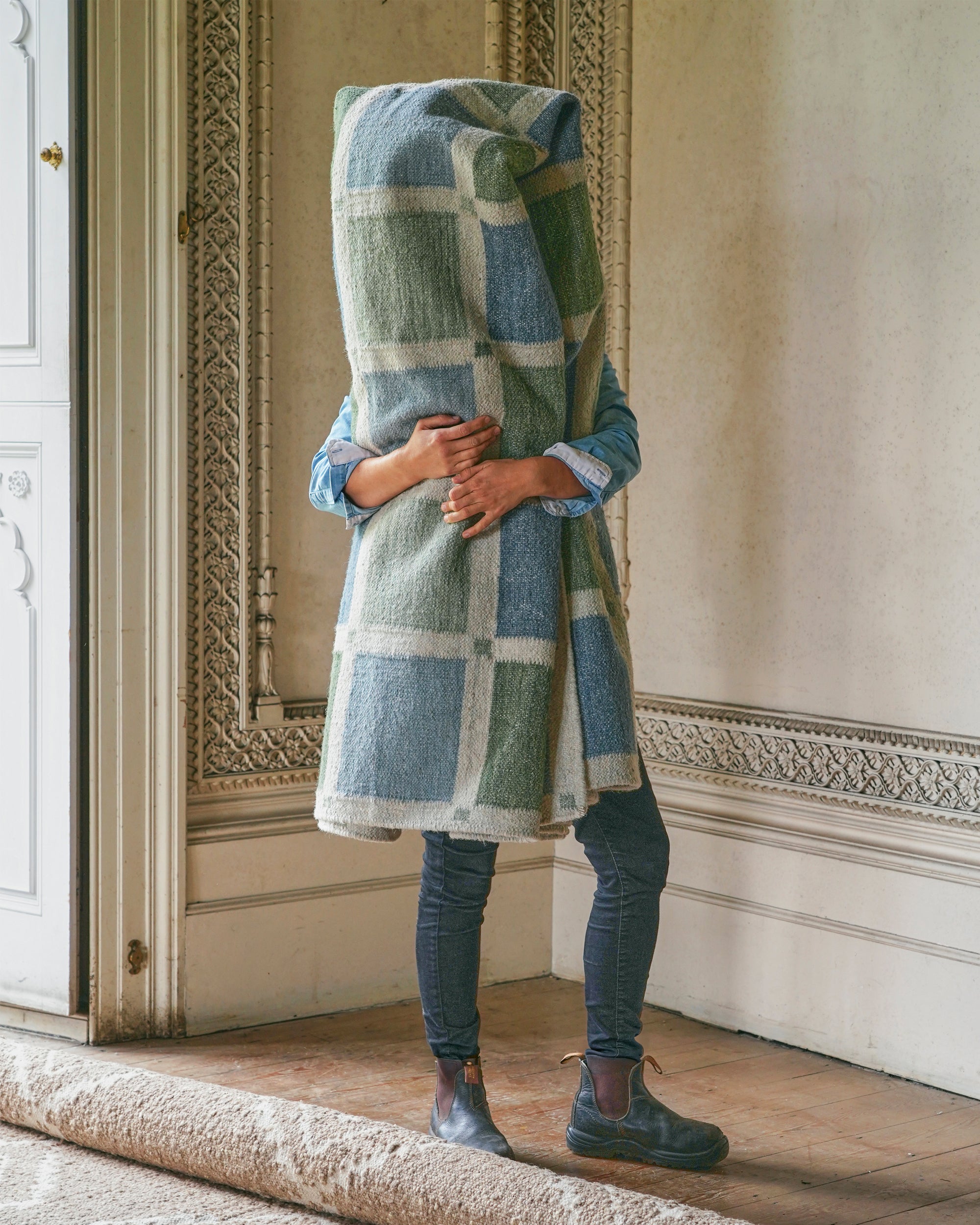 Person holding a blue and green checked rug in an elegant room.
