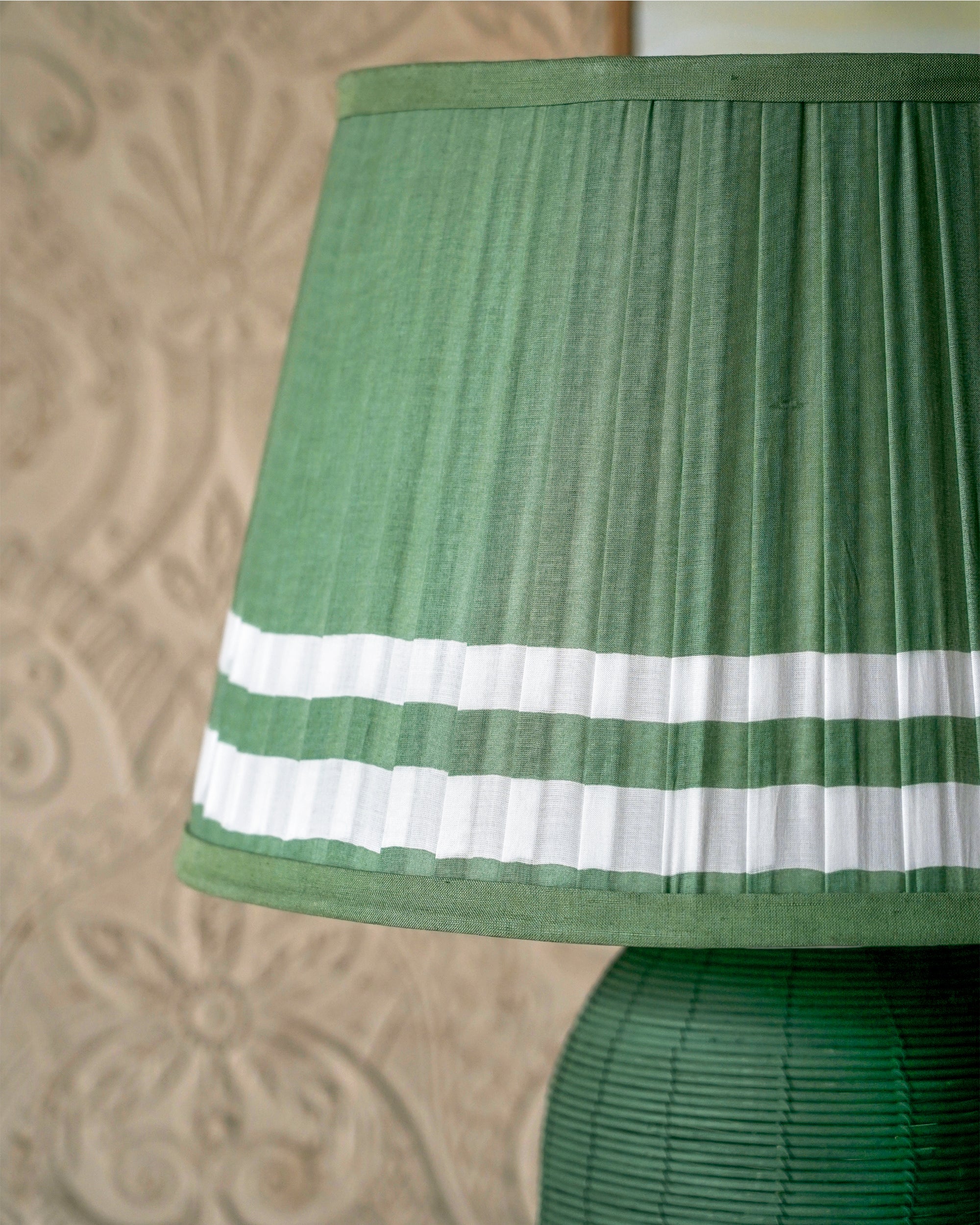 Green pleated lampshade against a textured beige wall