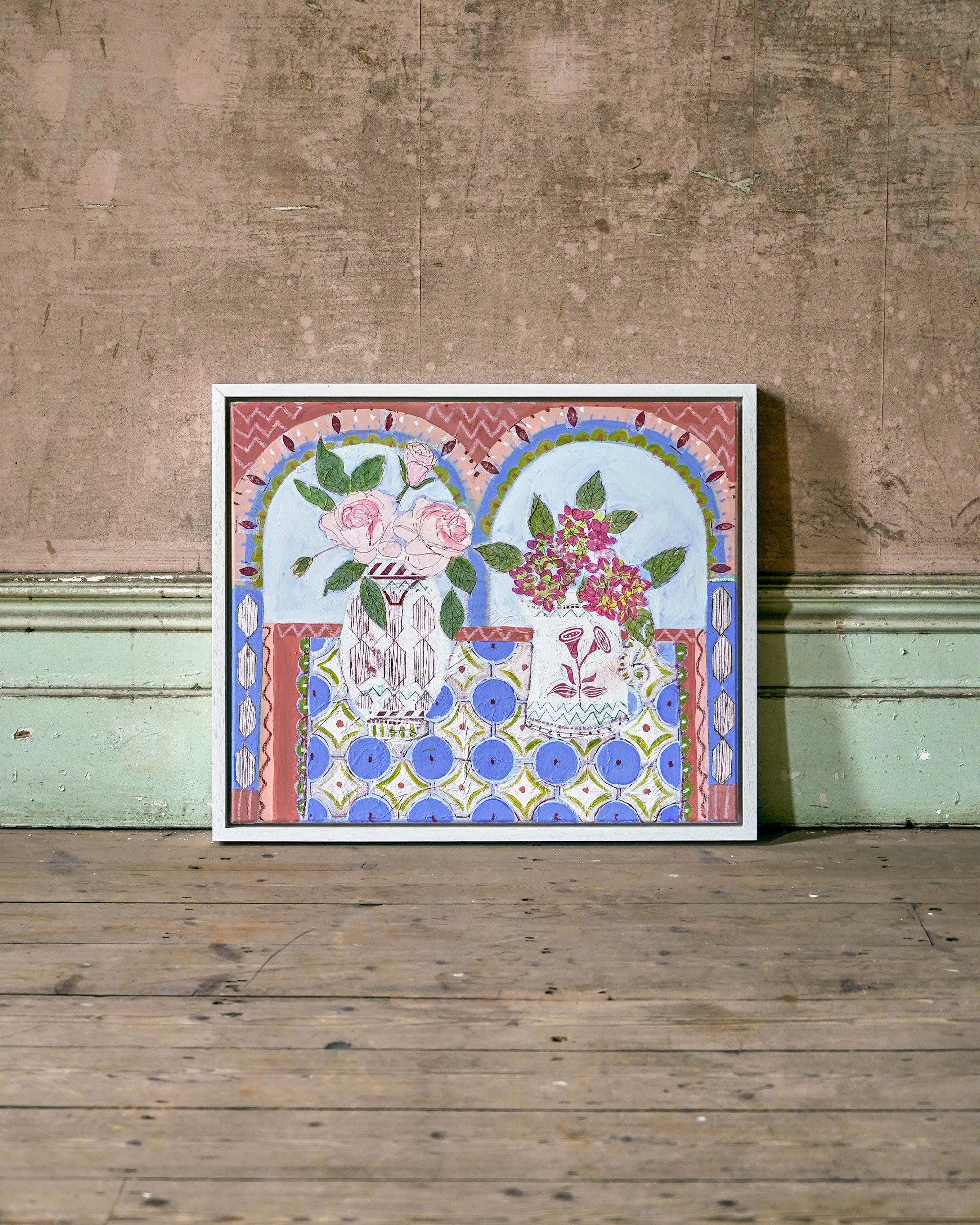 Decorative framed artwork with floral design on a wooden floor and wall.