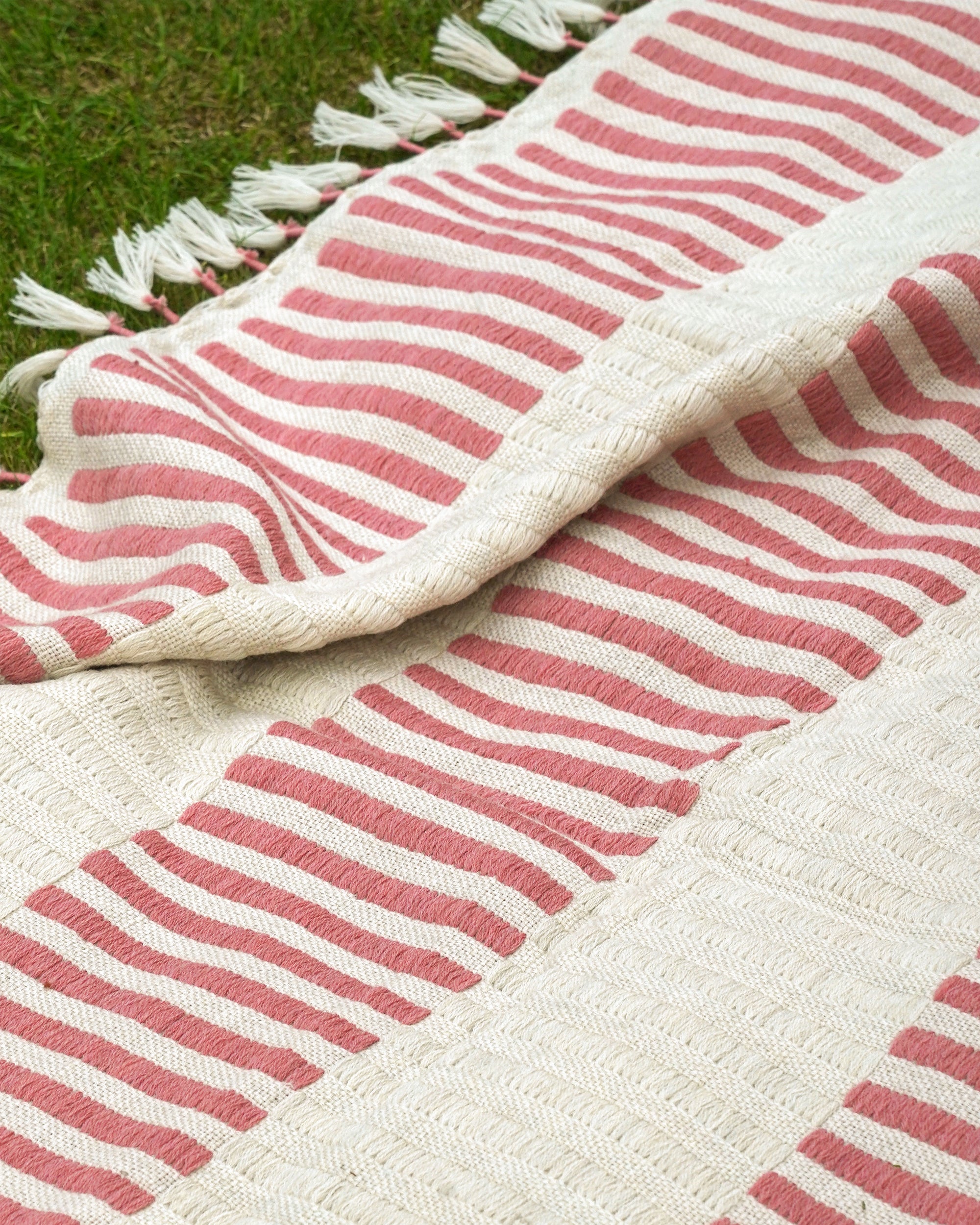 Close-up of a pink and white striped throw with tassels on a grassy background