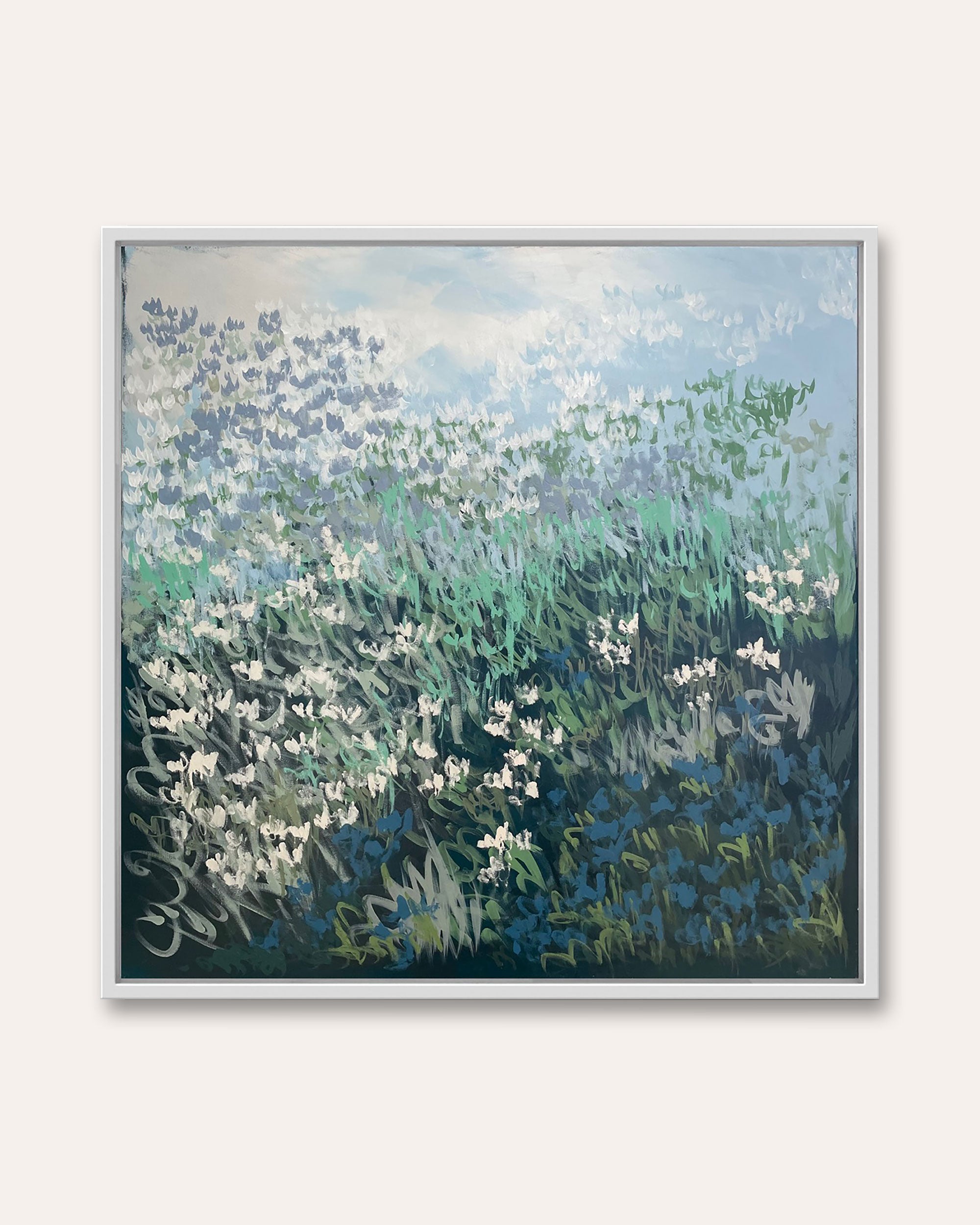 An impressionist-style framed painting depicting a field of white flowers and green foliage under a pale blue sky, mounted on a light beige wall.