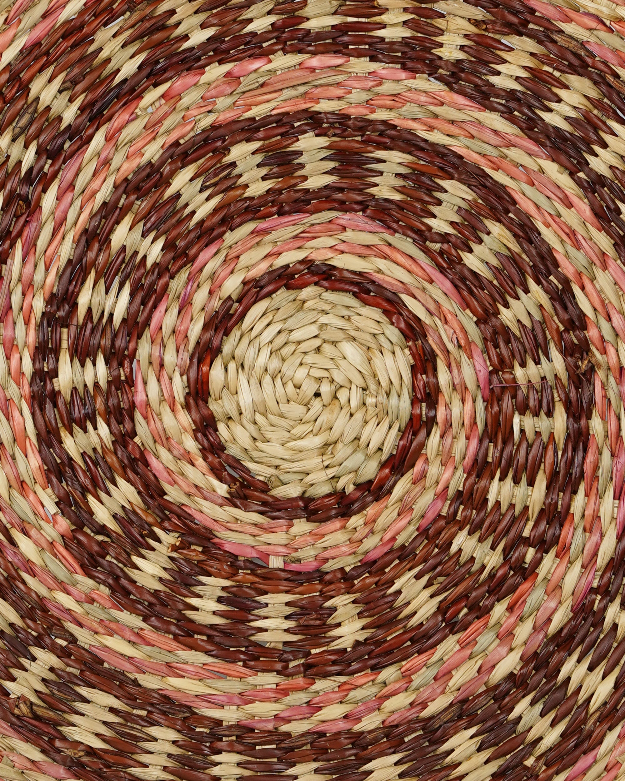 Close-up of a woven mat with concentric circle pattern in brown, beige, and pink.