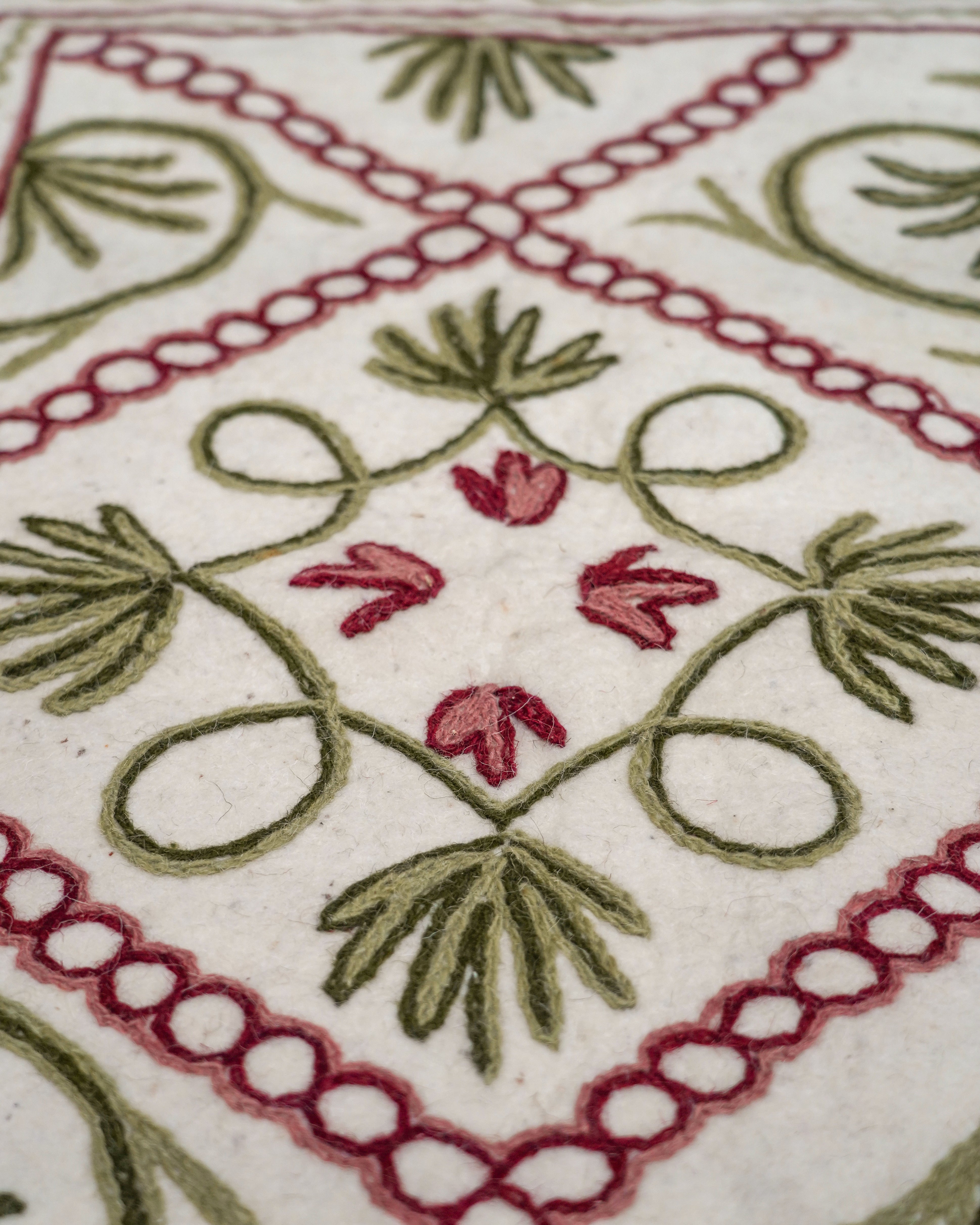 Close up detail image of the green and red Namda felt rug with geometric patterns