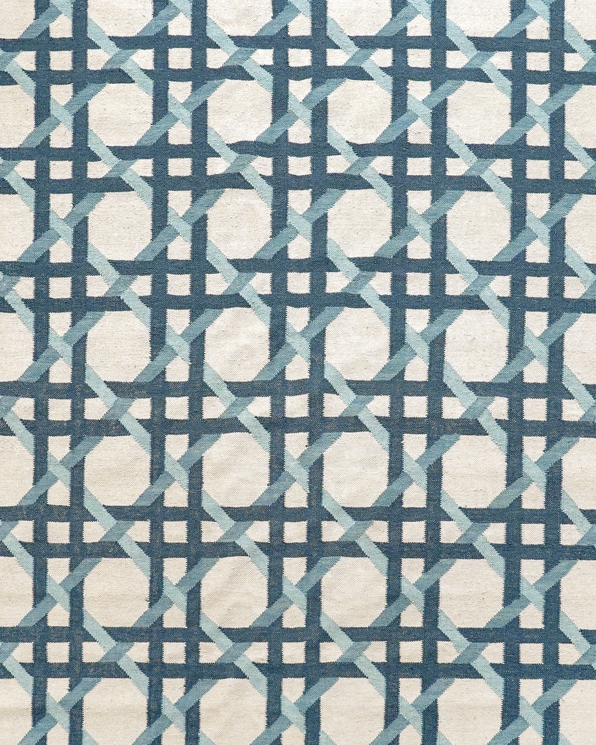 Close up detail of the Ganna Flat Weave Rug with blue and green geometric design on a beige background