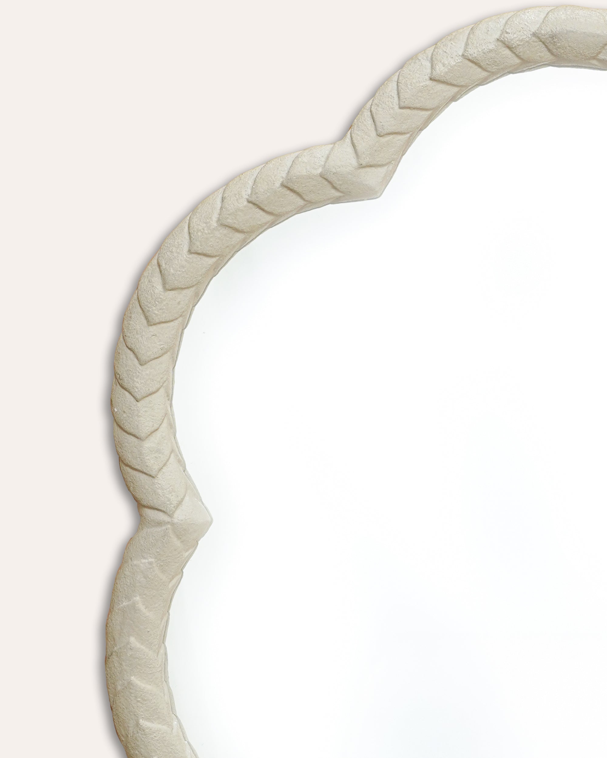 Scalloped mirror close up with a woven beige frame on a white background