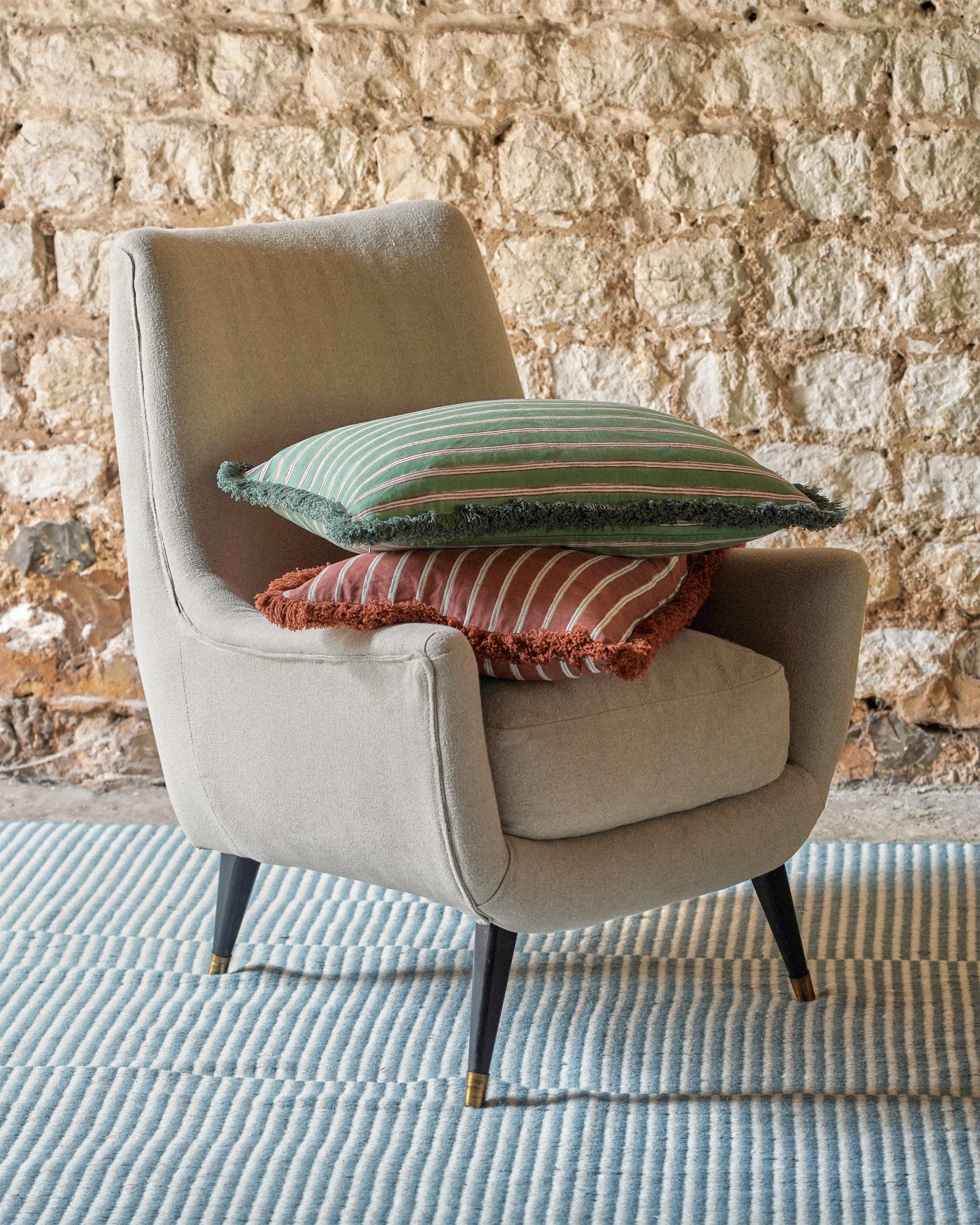 Beige armchair with decorative pillows against a stone wall.