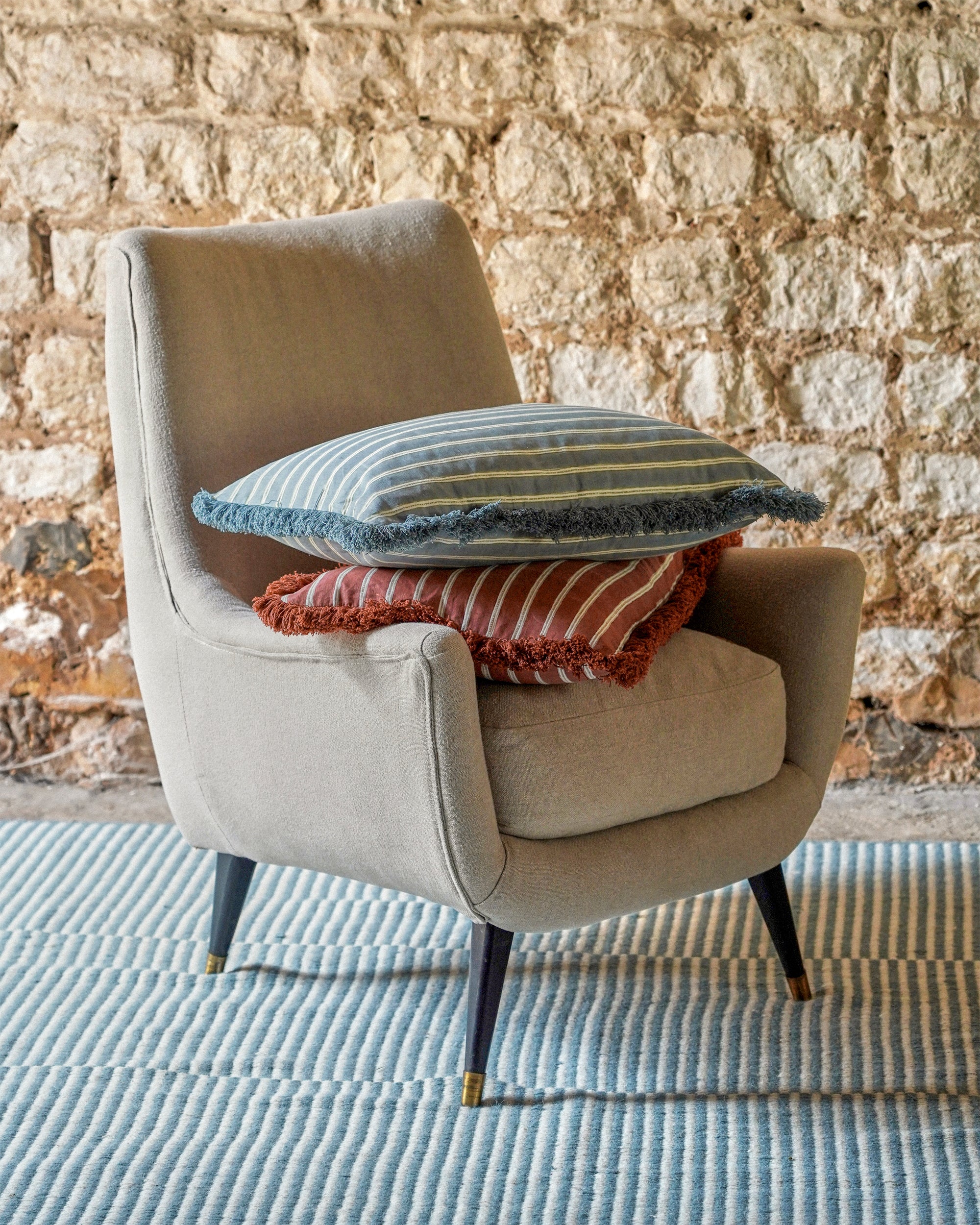 Beige armchair with decorative pillows against a stone wall.