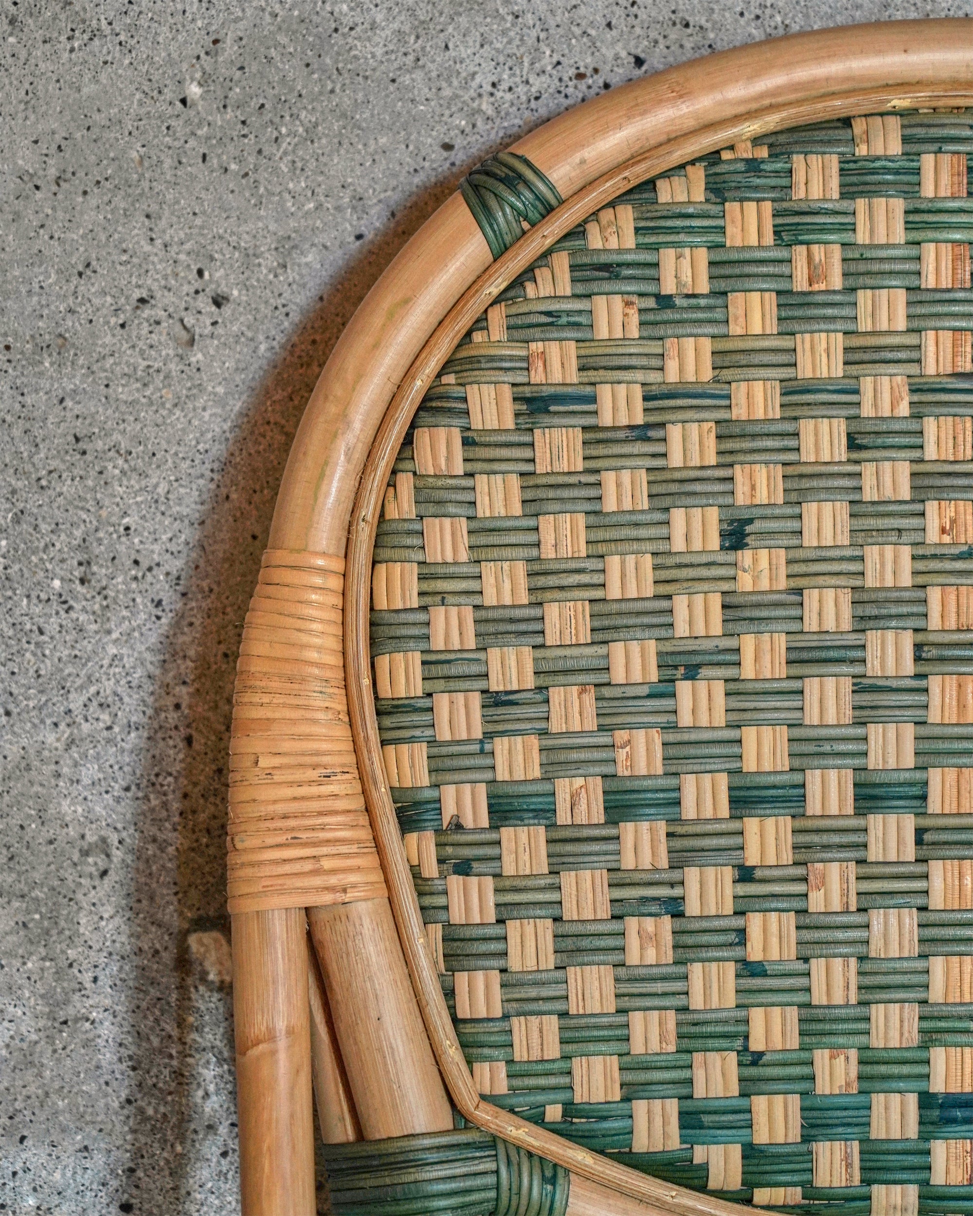 Close-up of a woven rattan chair with green and brown pattern on a concrete surface