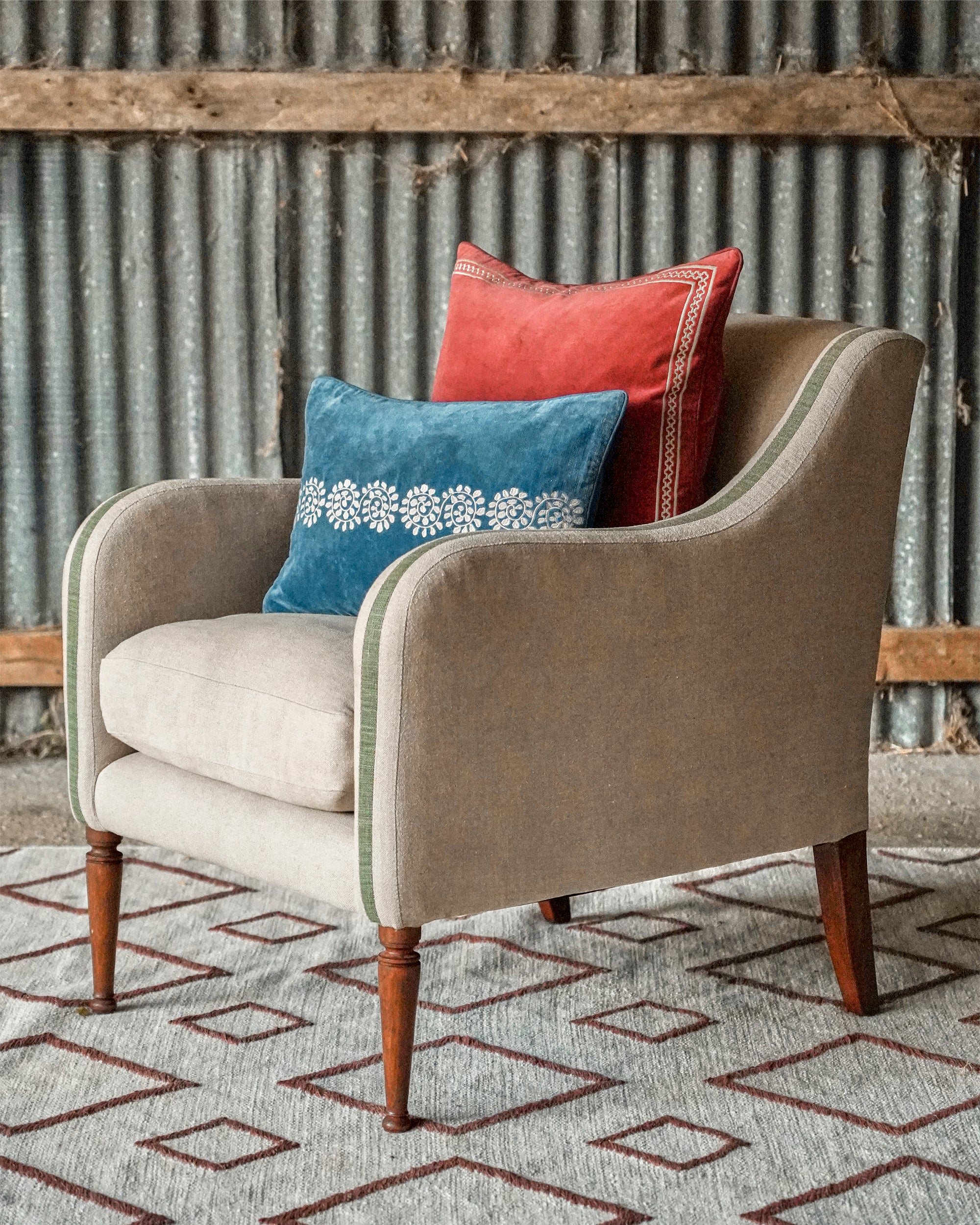 Beige armchair with blue and red cushions against a corrugated metal wall.