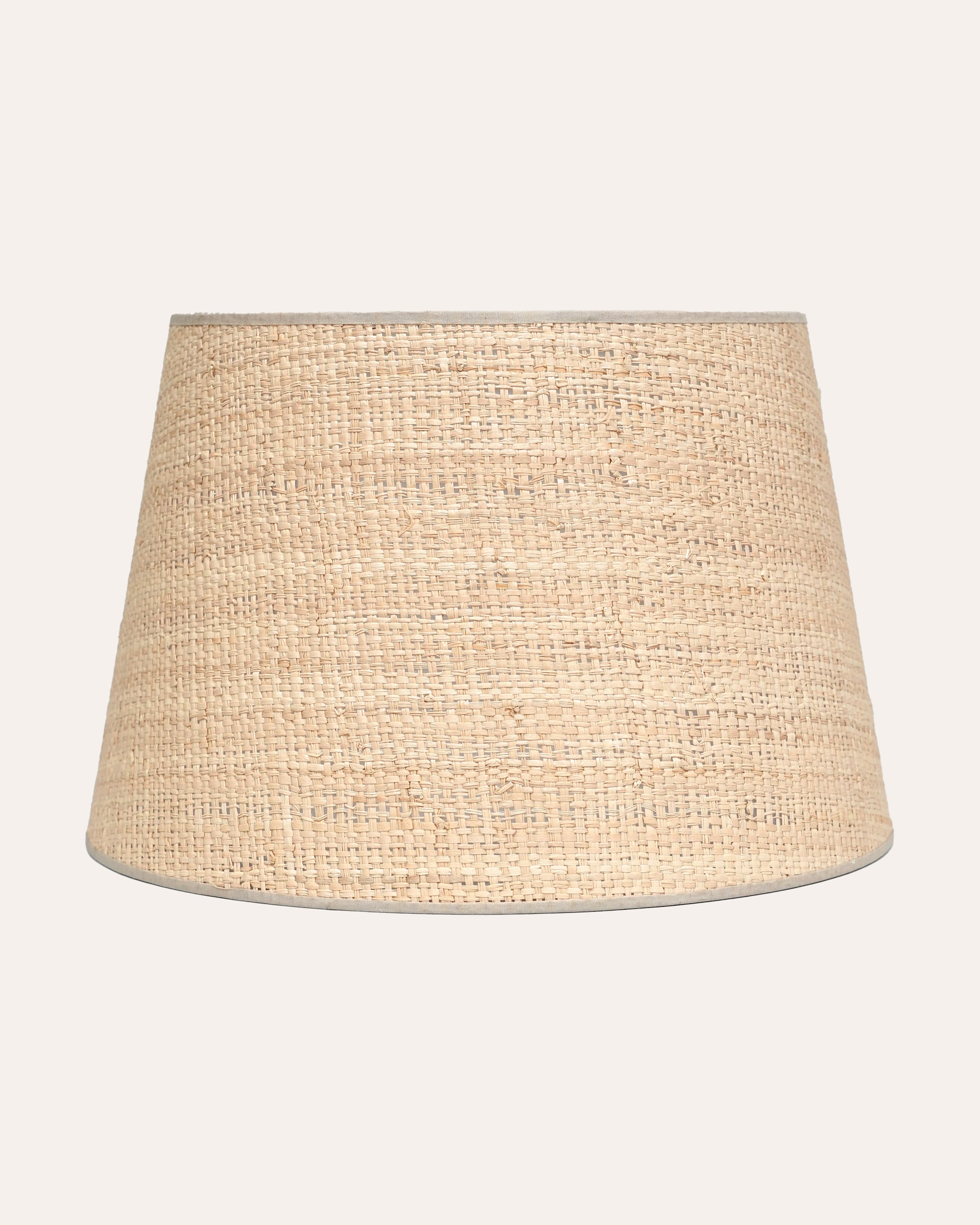 A beige raffia lampshade with a natural texture, cylindrical shape, and a subtle pattern.