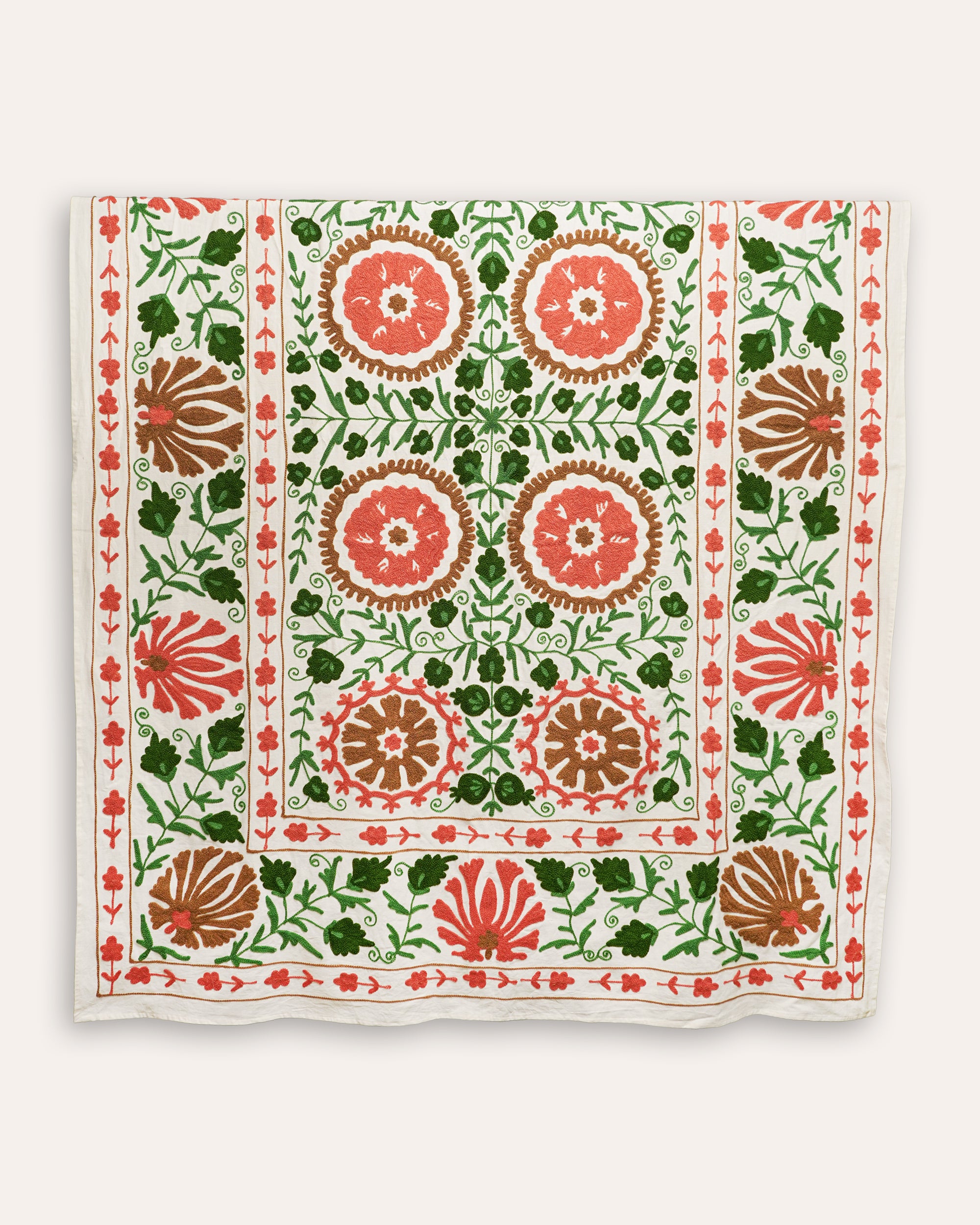 An embroidered Suzani throw featuring a geometric pattern with circles and floral motifs, predominantly in green and red colors on a white background.