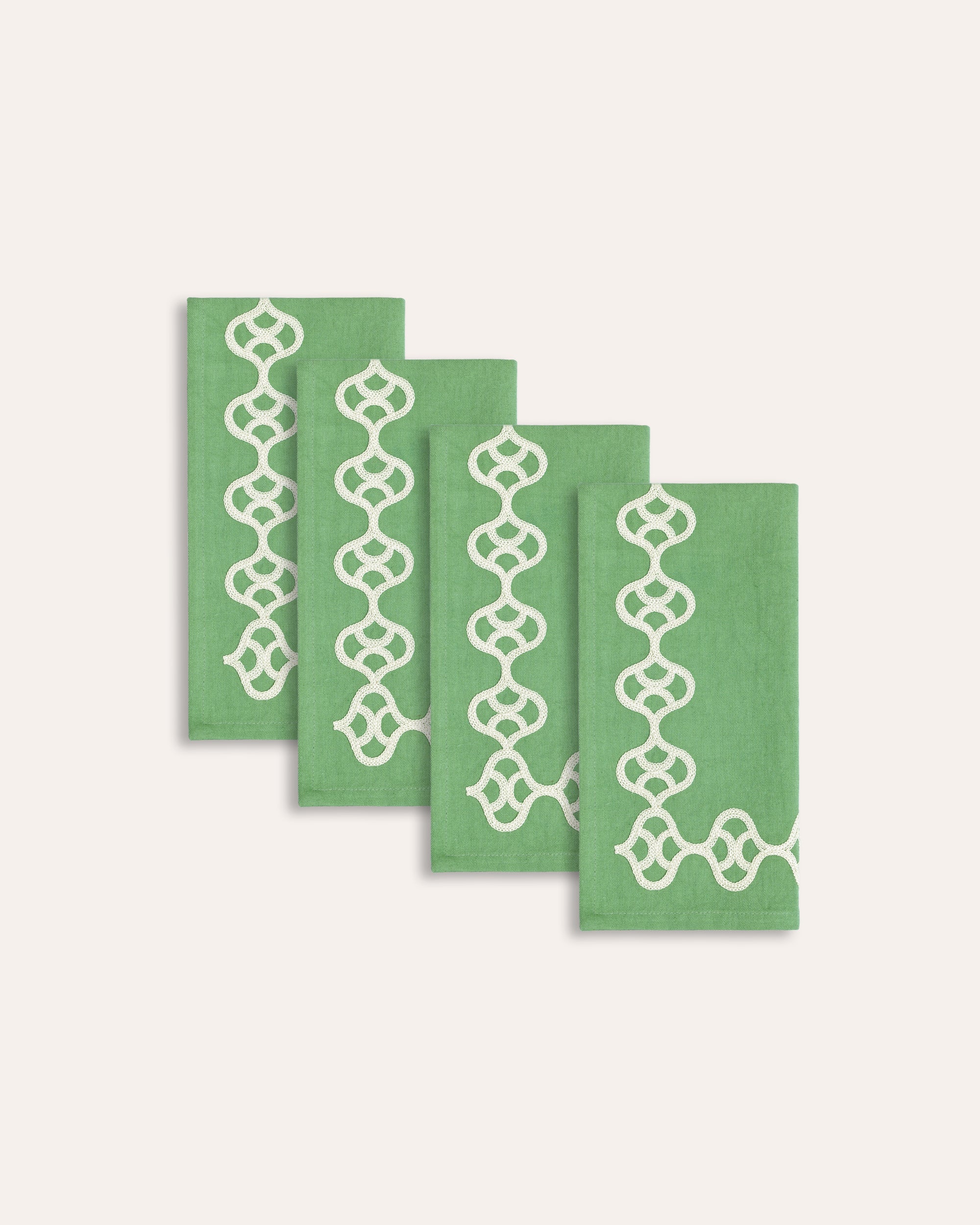 Four green napkins with white geometric patterns on a white background