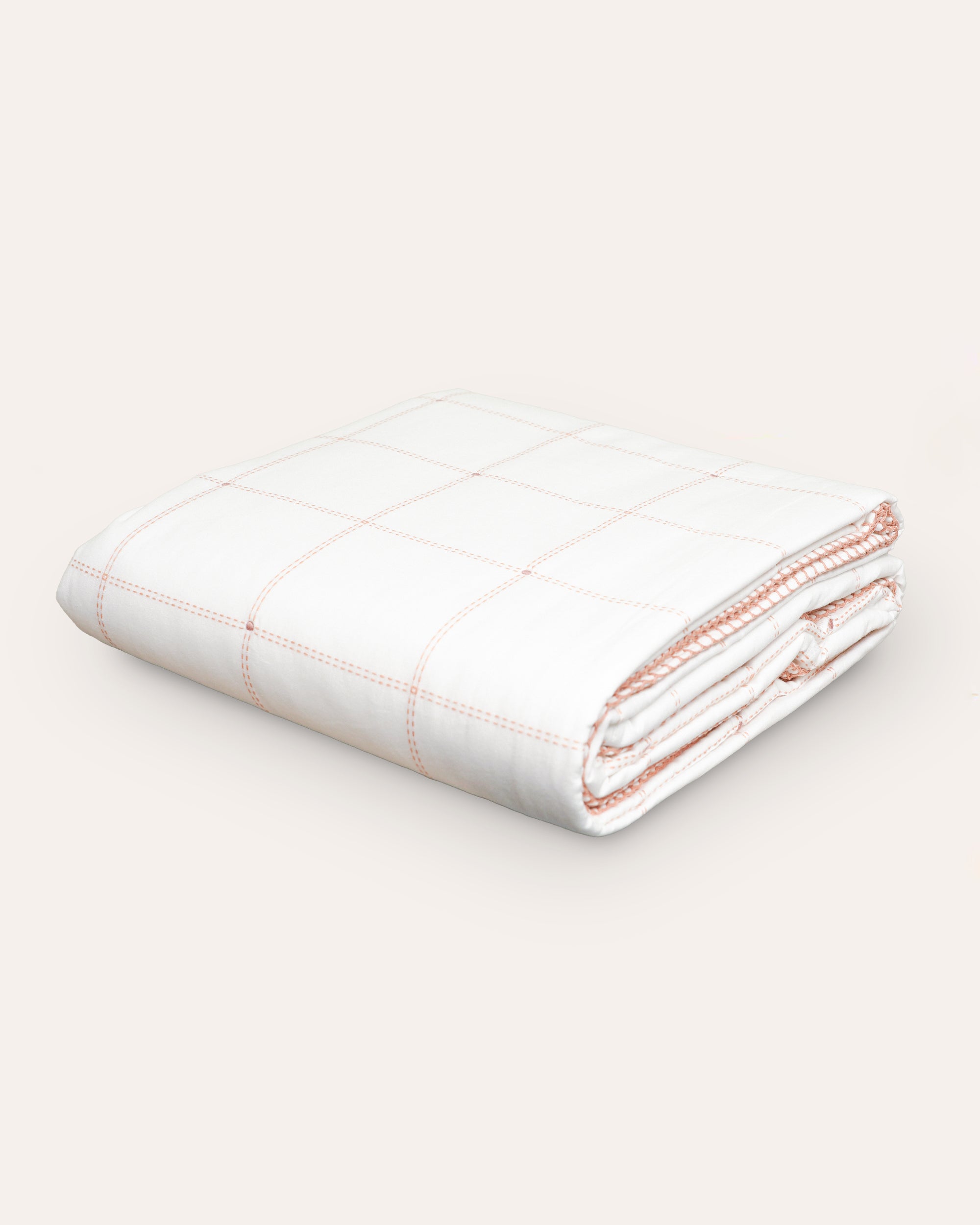 A folded quilted bedspread with a subtle embroidered square pattern in a pink hue.