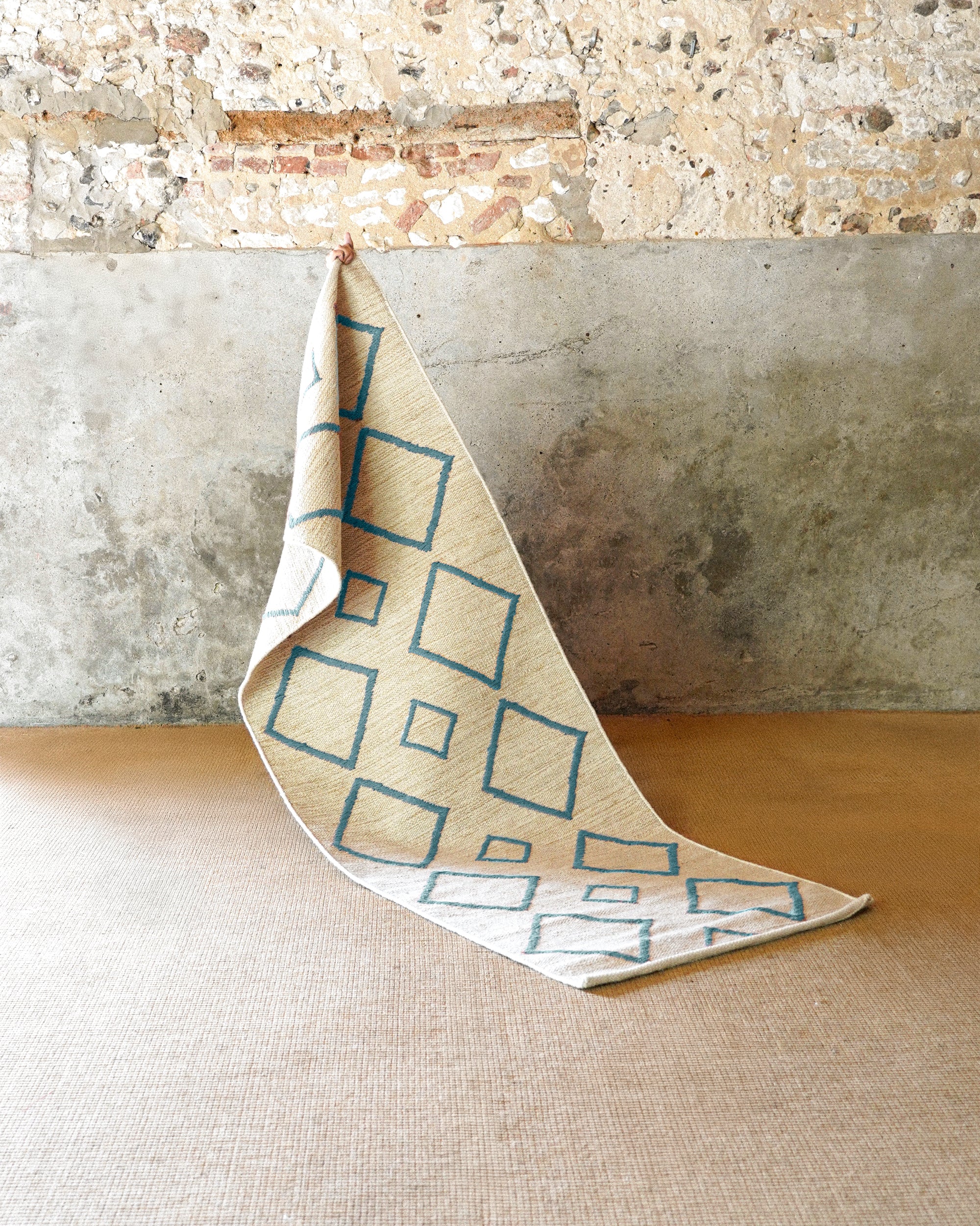 Folded fabric with geometric pattern against a textured wall and wooden floor.