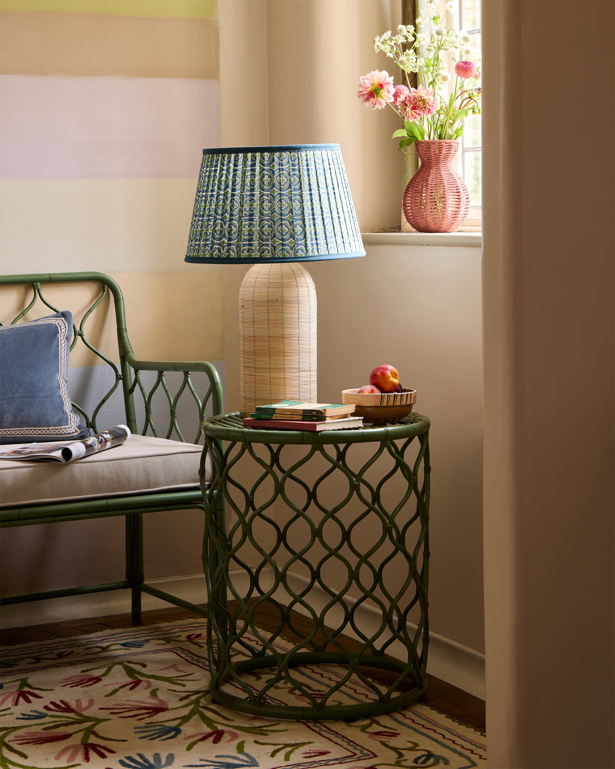 Green metal side table with a lamp and decorative items in a room with a chair and floral arrangement.