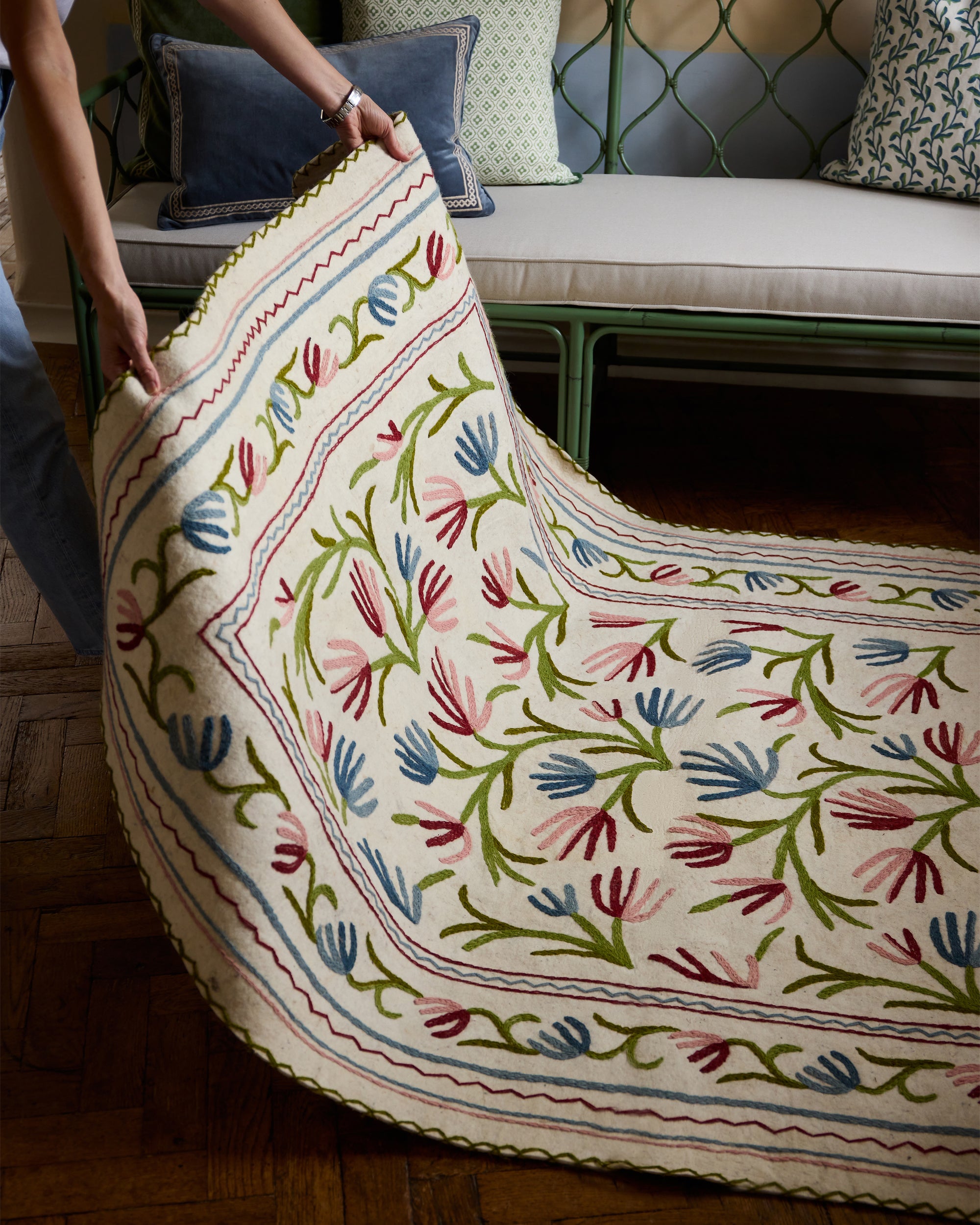 Person holding a colorful embroidered felt rug with floral patterns in a room.