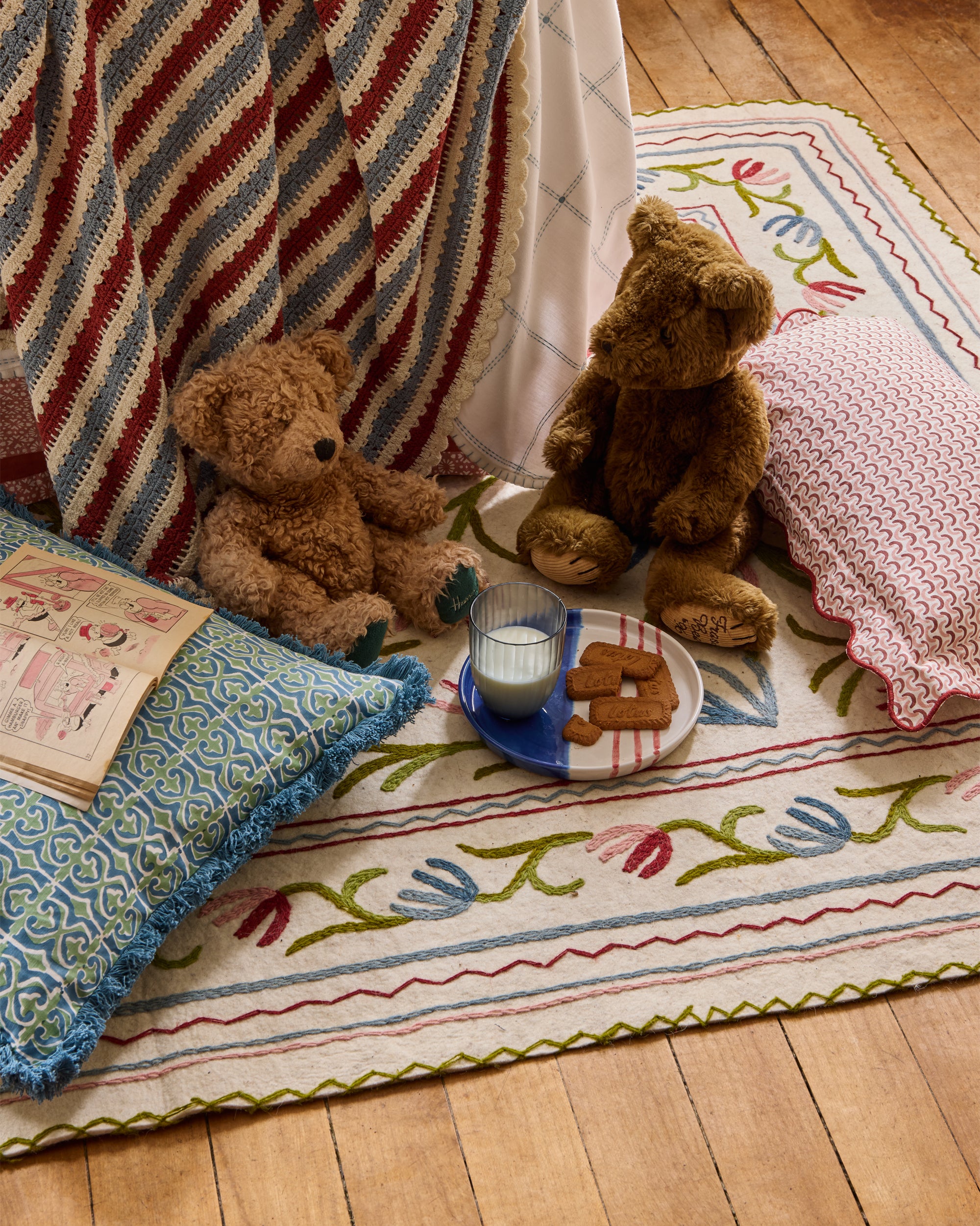 Two teddy bears sitting on a colorful rug with a plate of cookies and a book.