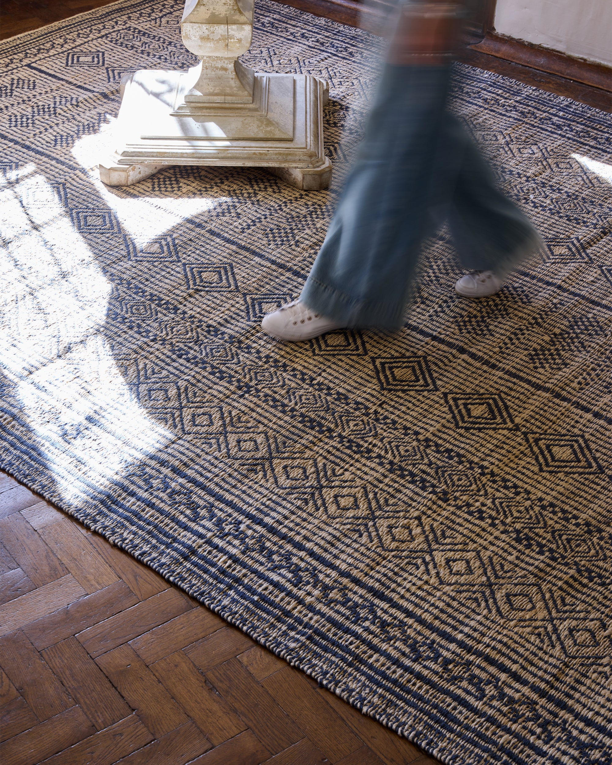Person walking on a geometric patterned blue rug with a wooden table in the foreground