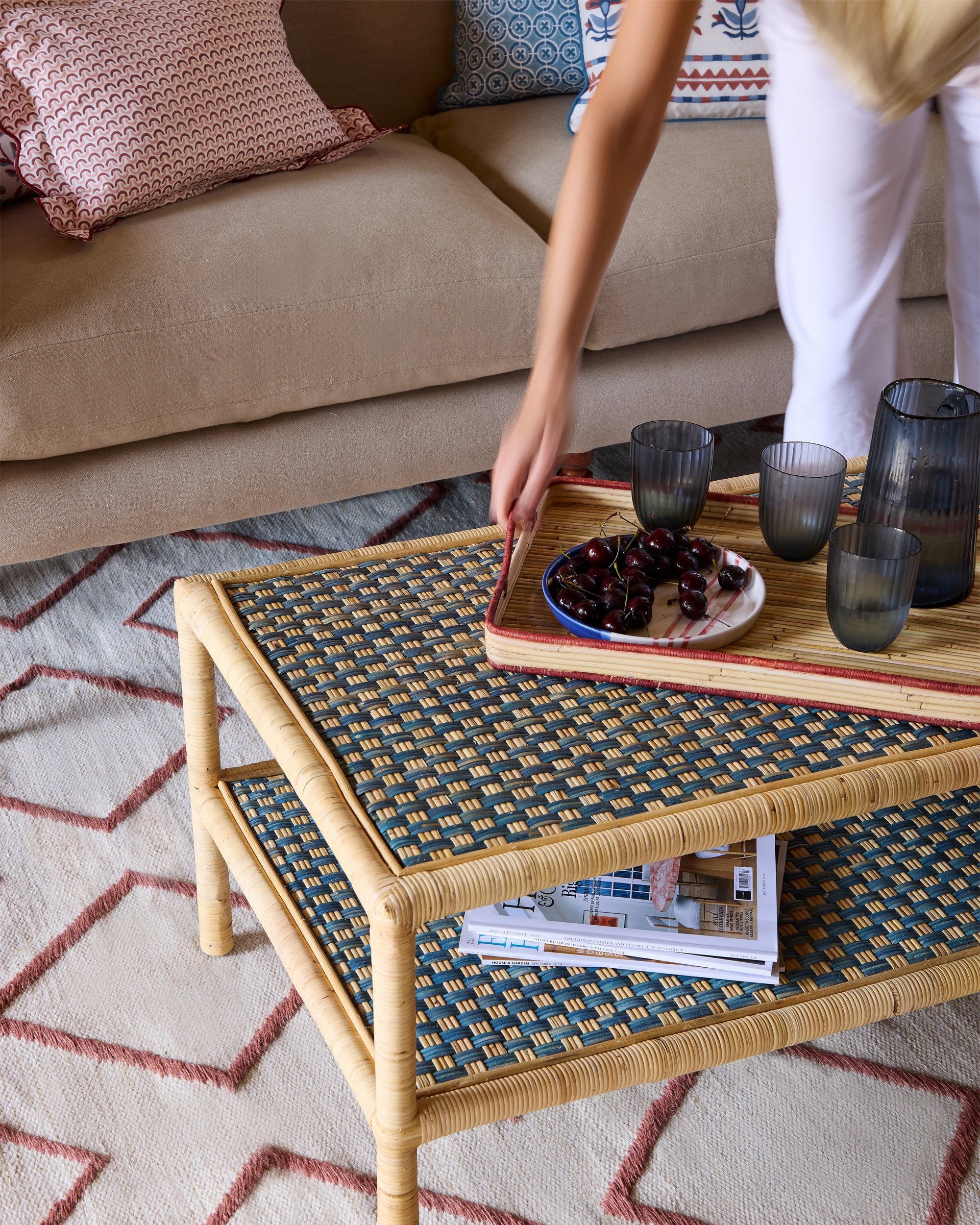 Person placing a red rattan tray down on a blue rattan coffee table in a living room.
