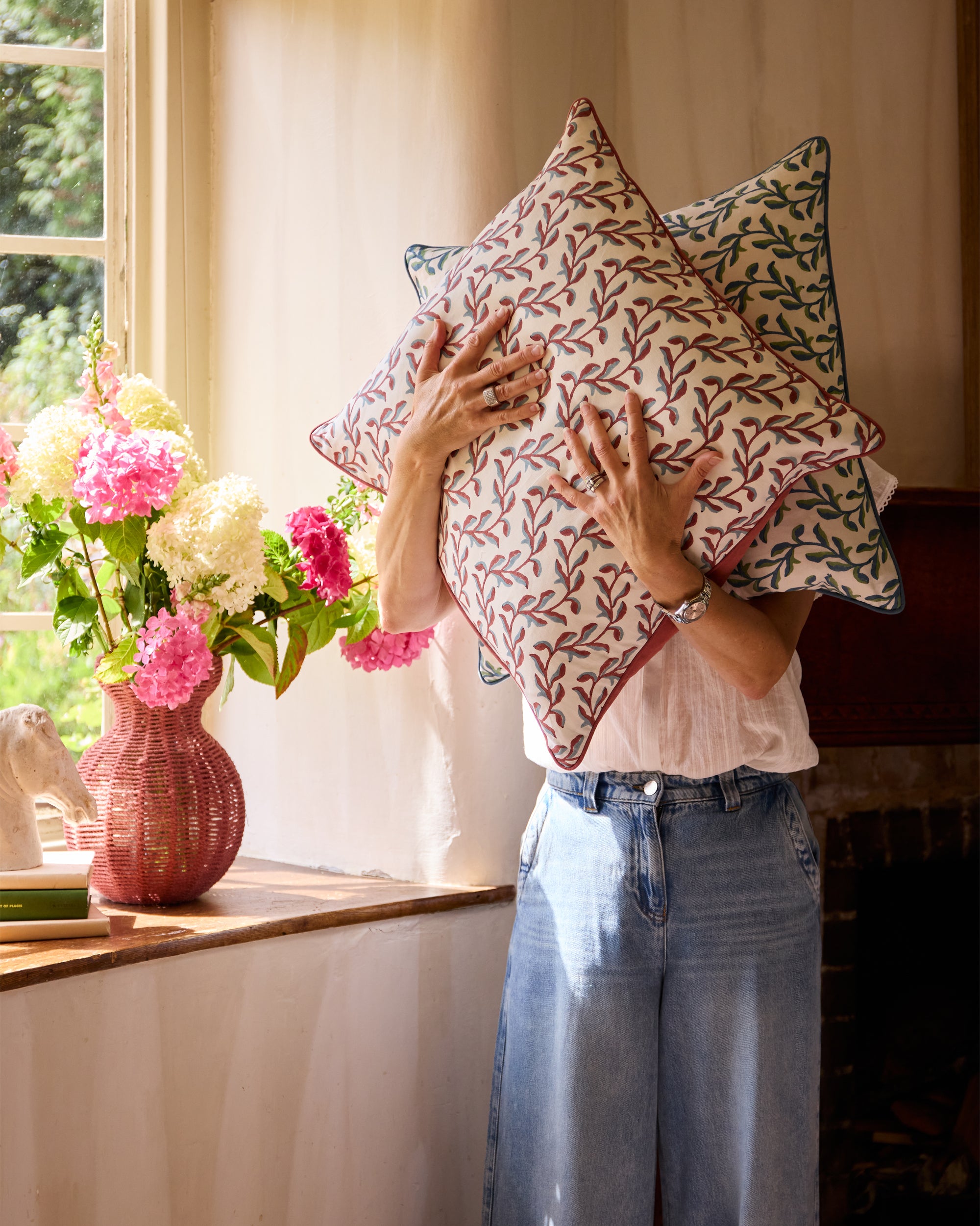 Lifestyle image of someone showcasing the two colour ways of the Mariana floral print cushion