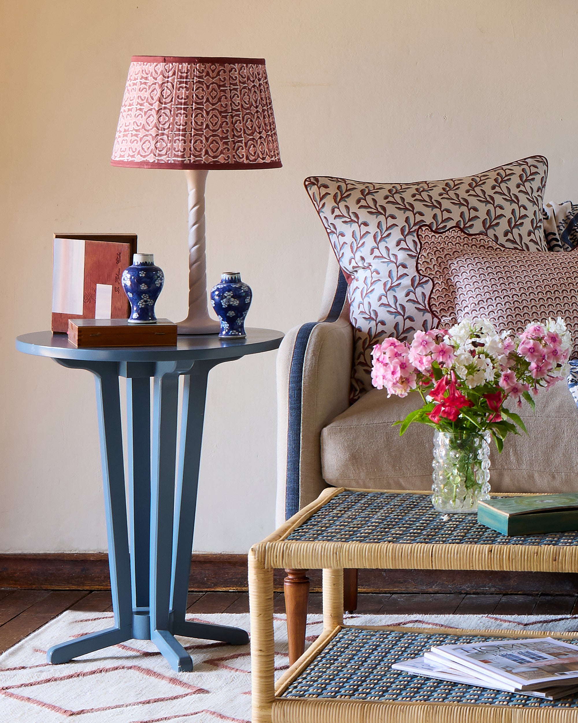 Living room with a side table, lamp, and sofa with decorative pillows and flowers.
