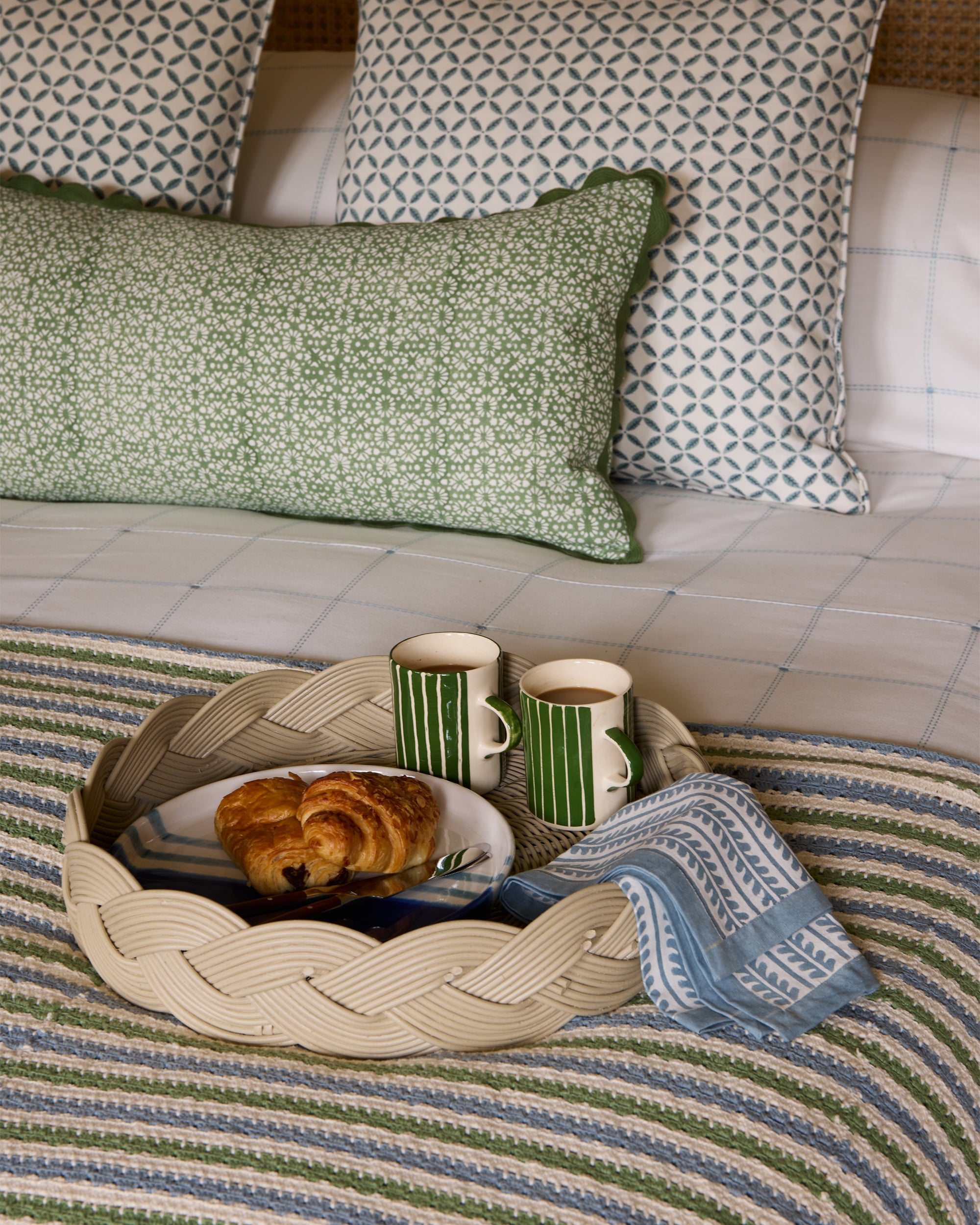 Tray with food and drinks on a bed with patterned pillows and blanket