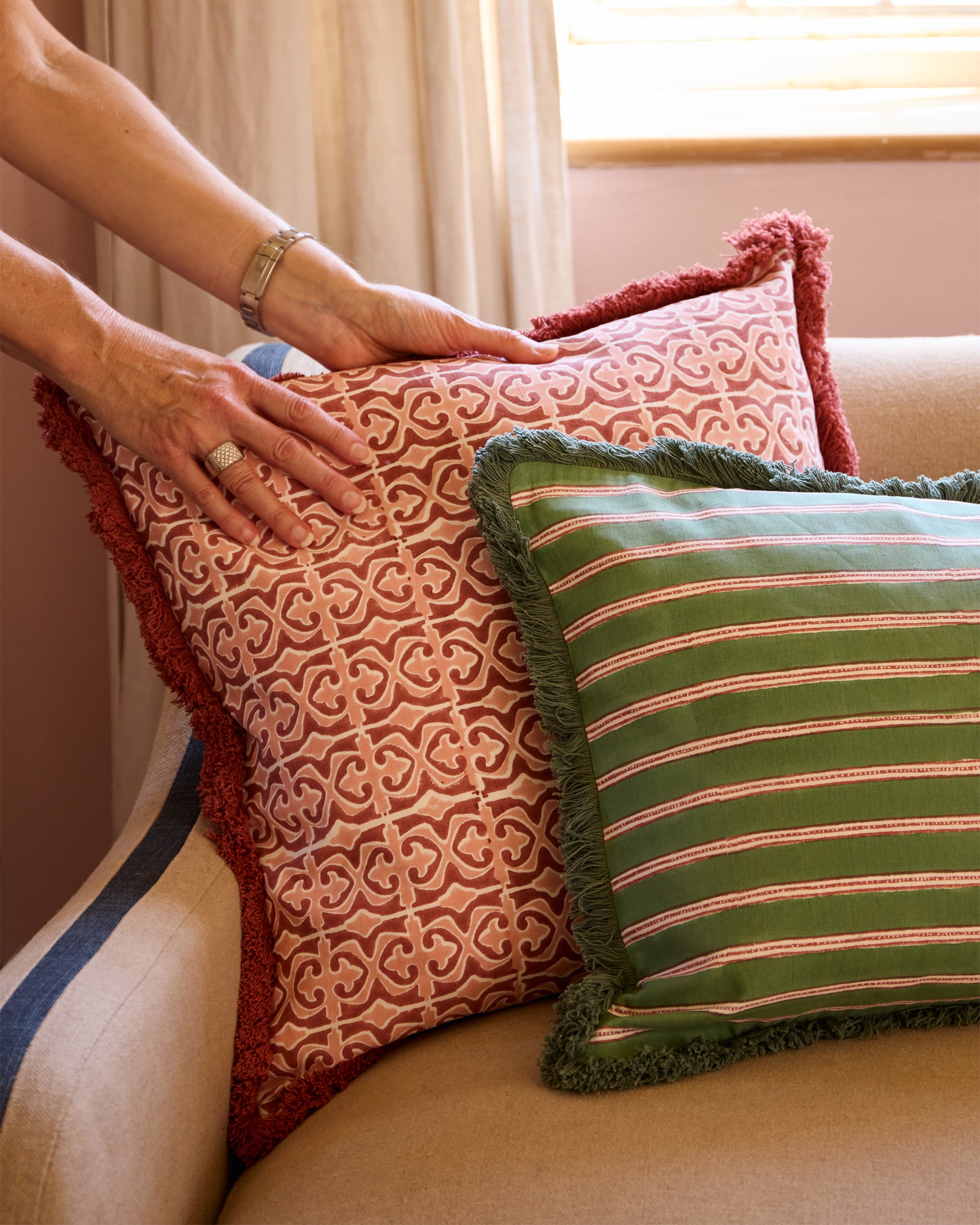 Person arranging patterned cushions on a sofa with a neutral background
