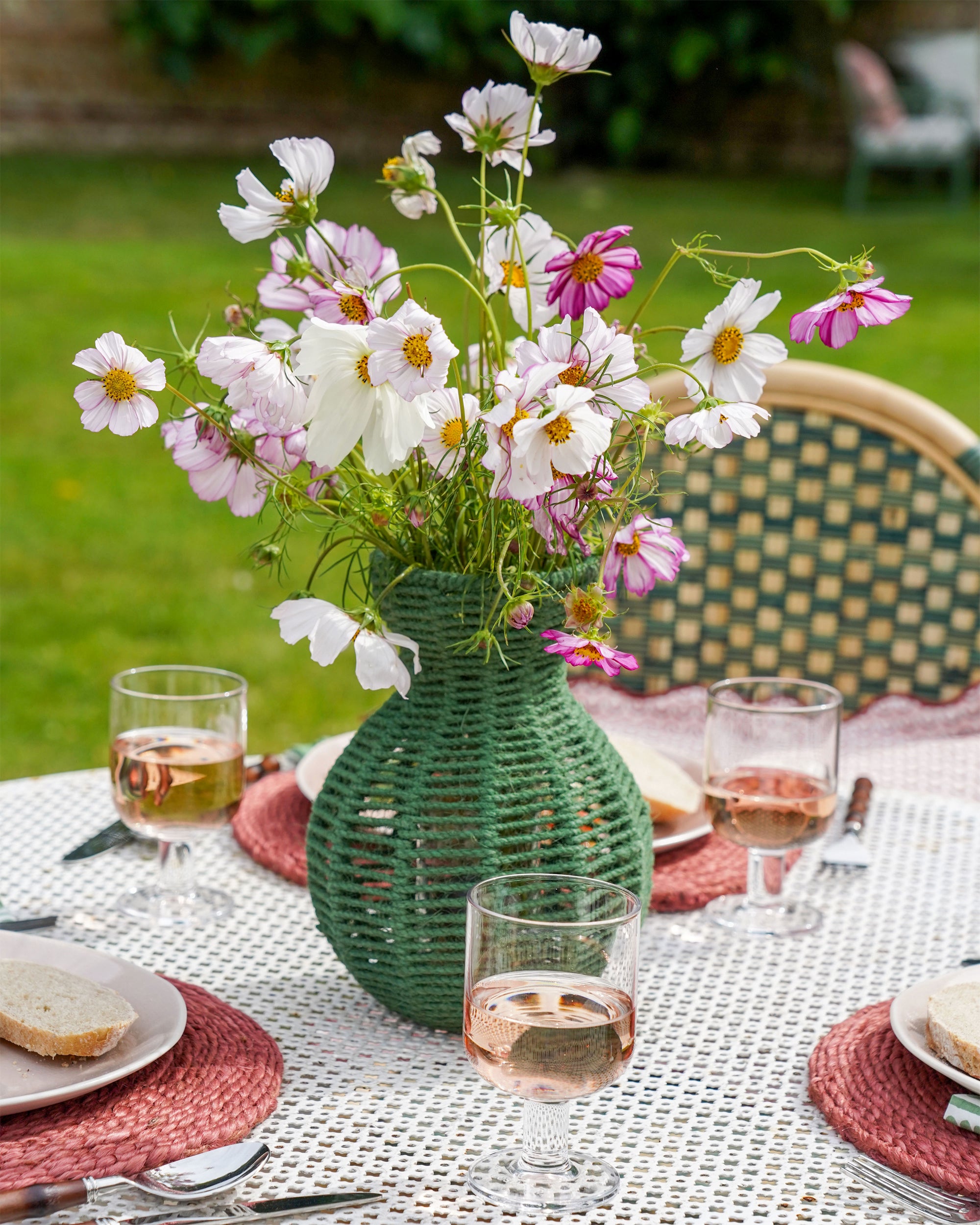 Green woven vase with flowers on a table set outdoors