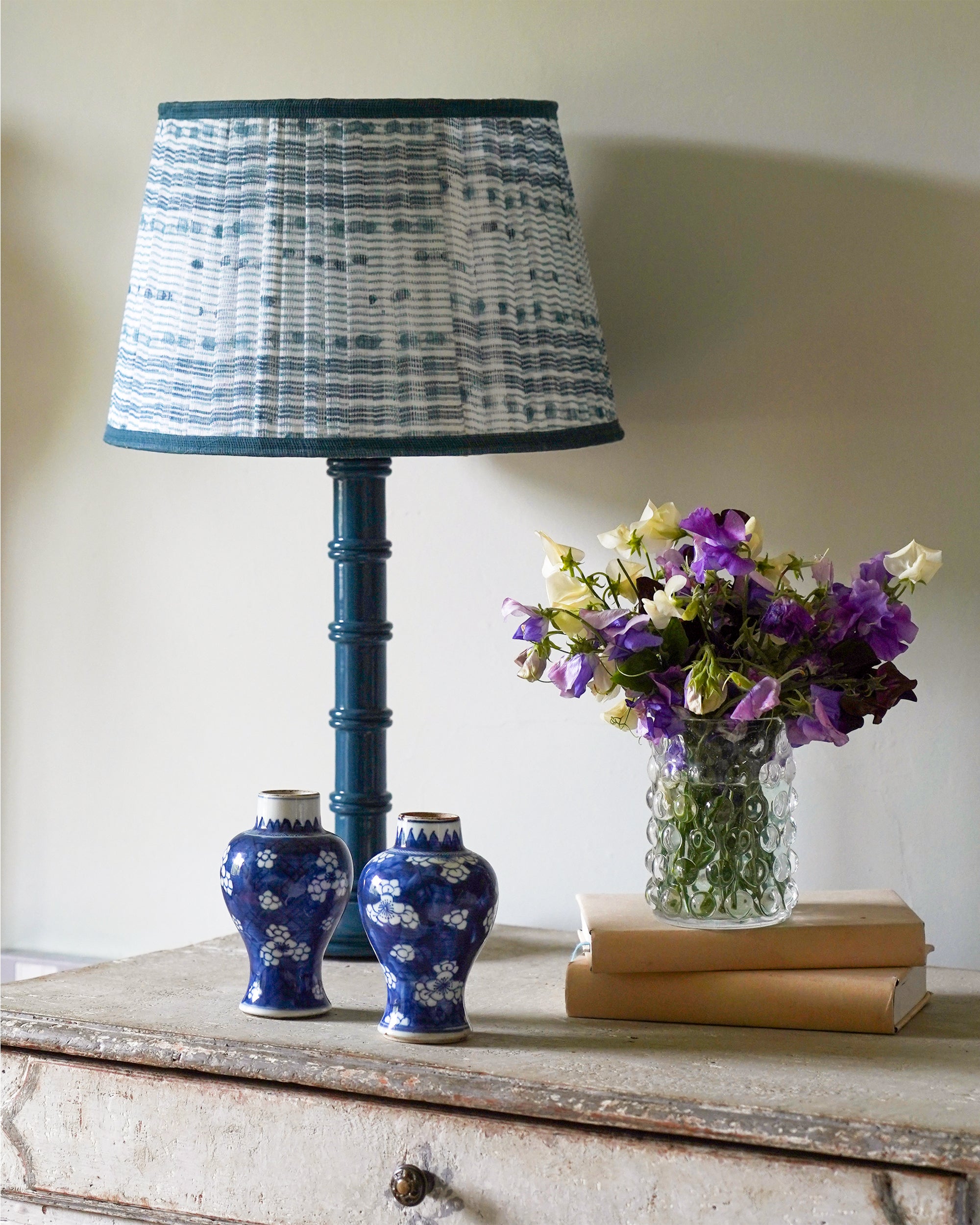 Decorative lamp with a checkered shade, two blue vases, and a vase of flowers on a wooden surface.