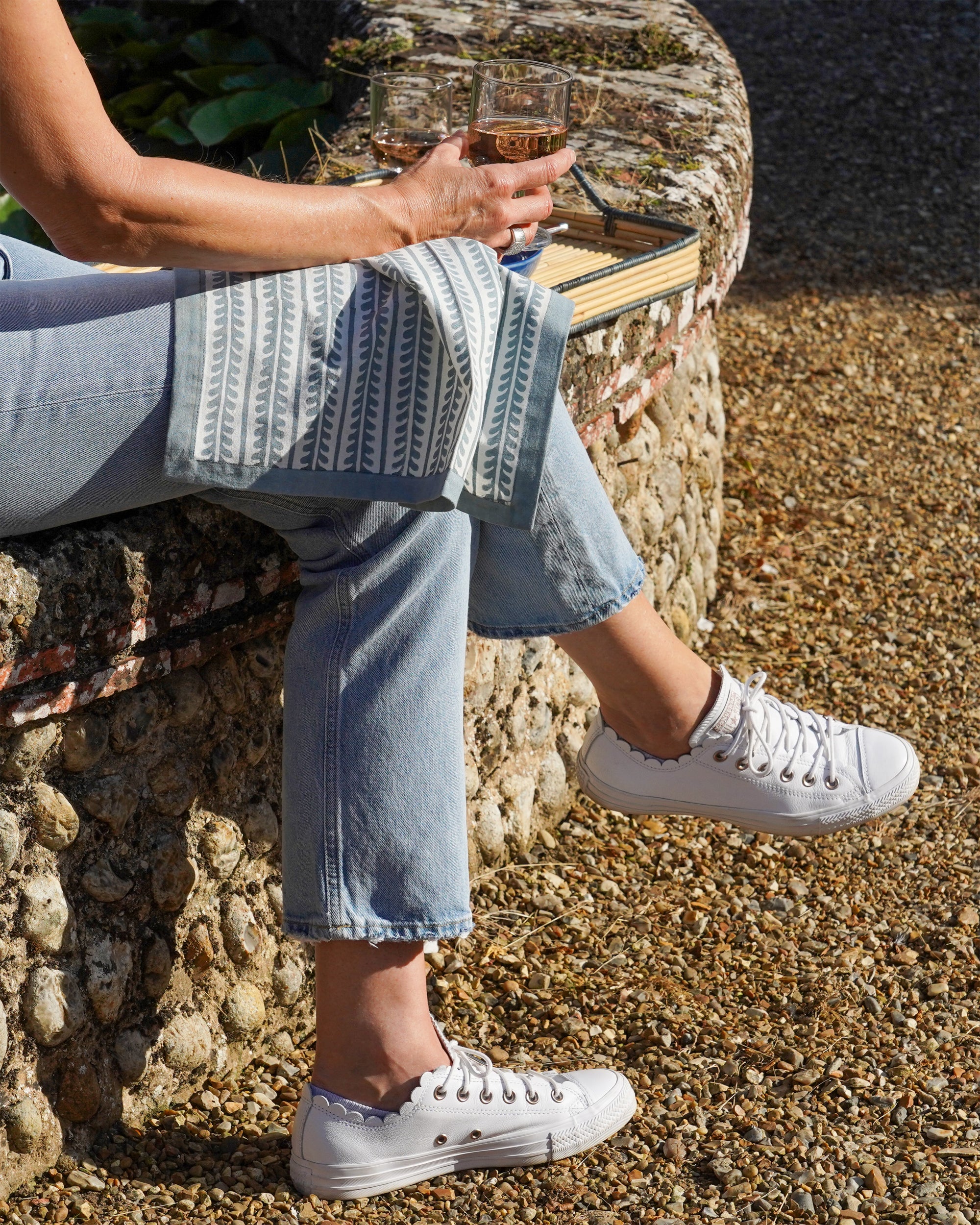 Person wearing white trainers and light blue jeans sitting on a stone wall outdoors with a blue bel napkin on her knee