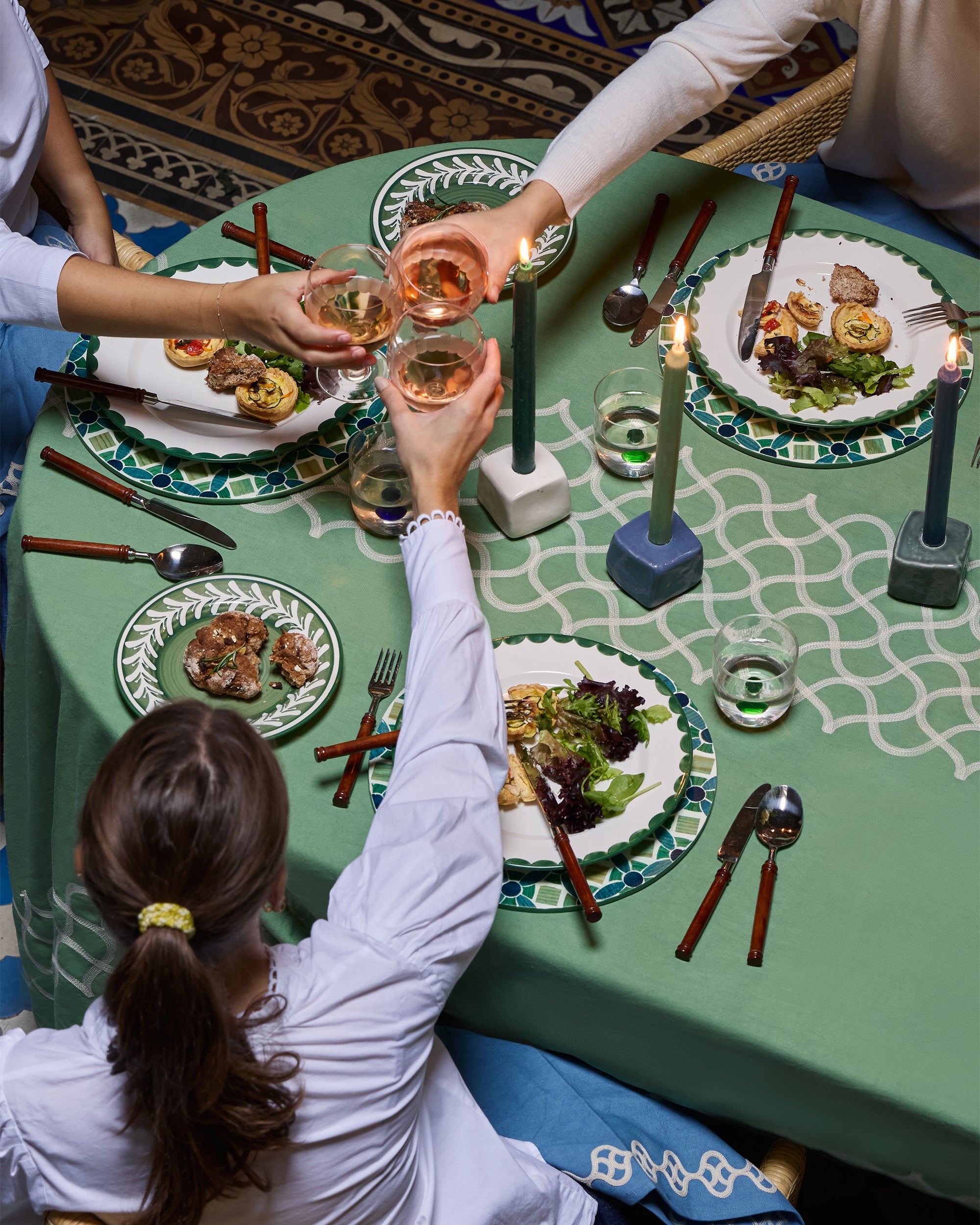 People toasting with glasses at a dining table set with plates, utensils, and candles.