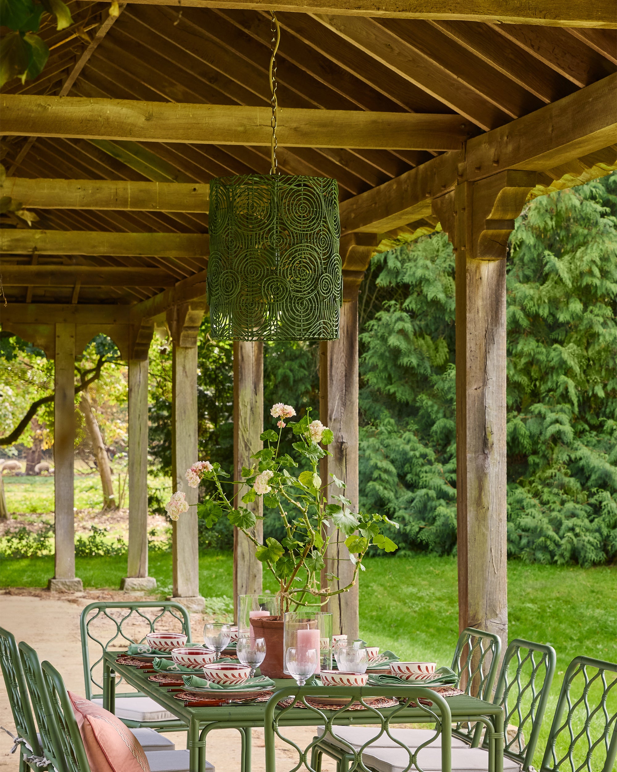 Outdoor setting with a green table and chairs under a wooden pergola, surrounded by greenery.