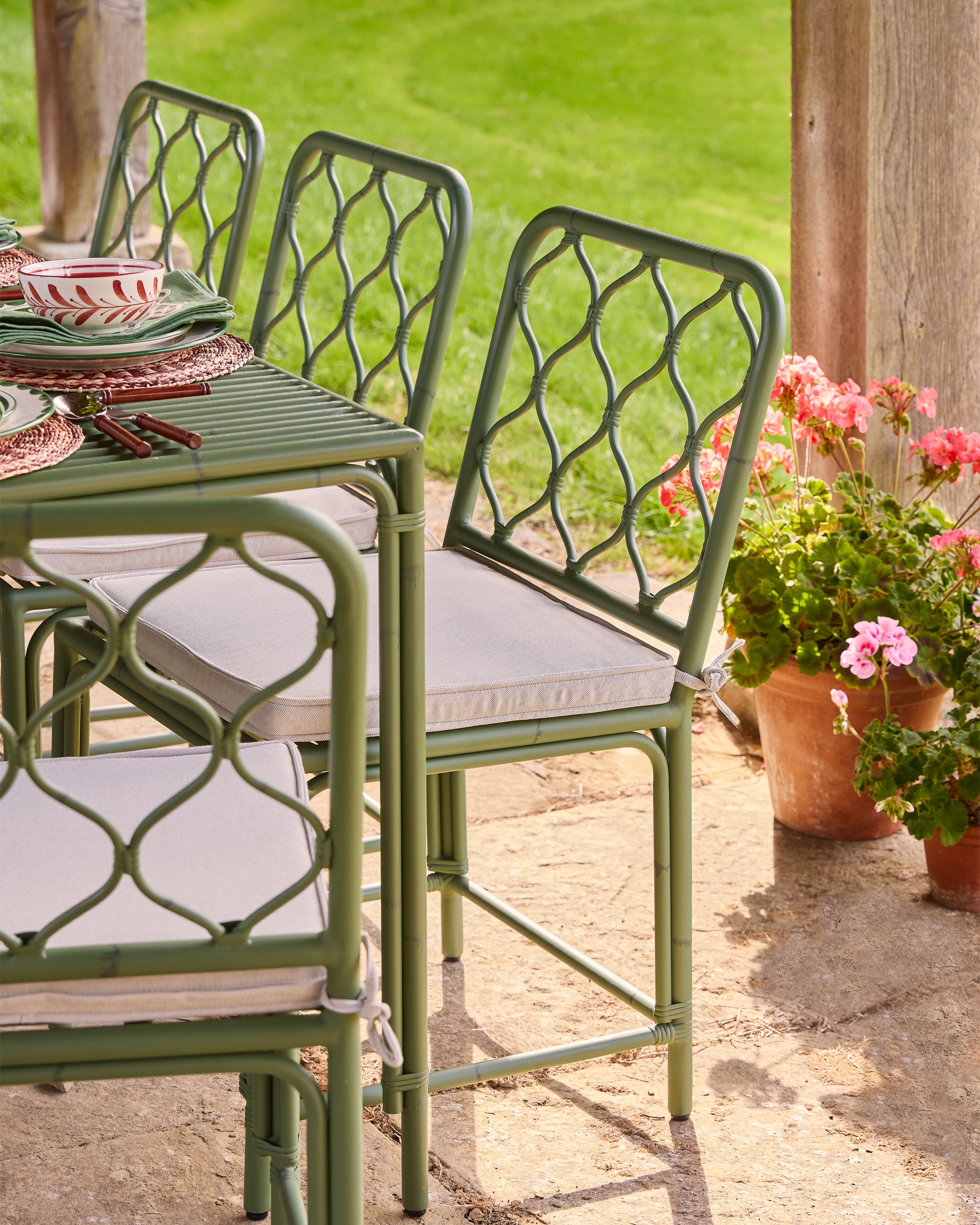 Outdoor patio set with green metal chairs and table on a stone patio, surrounded by potted plants.