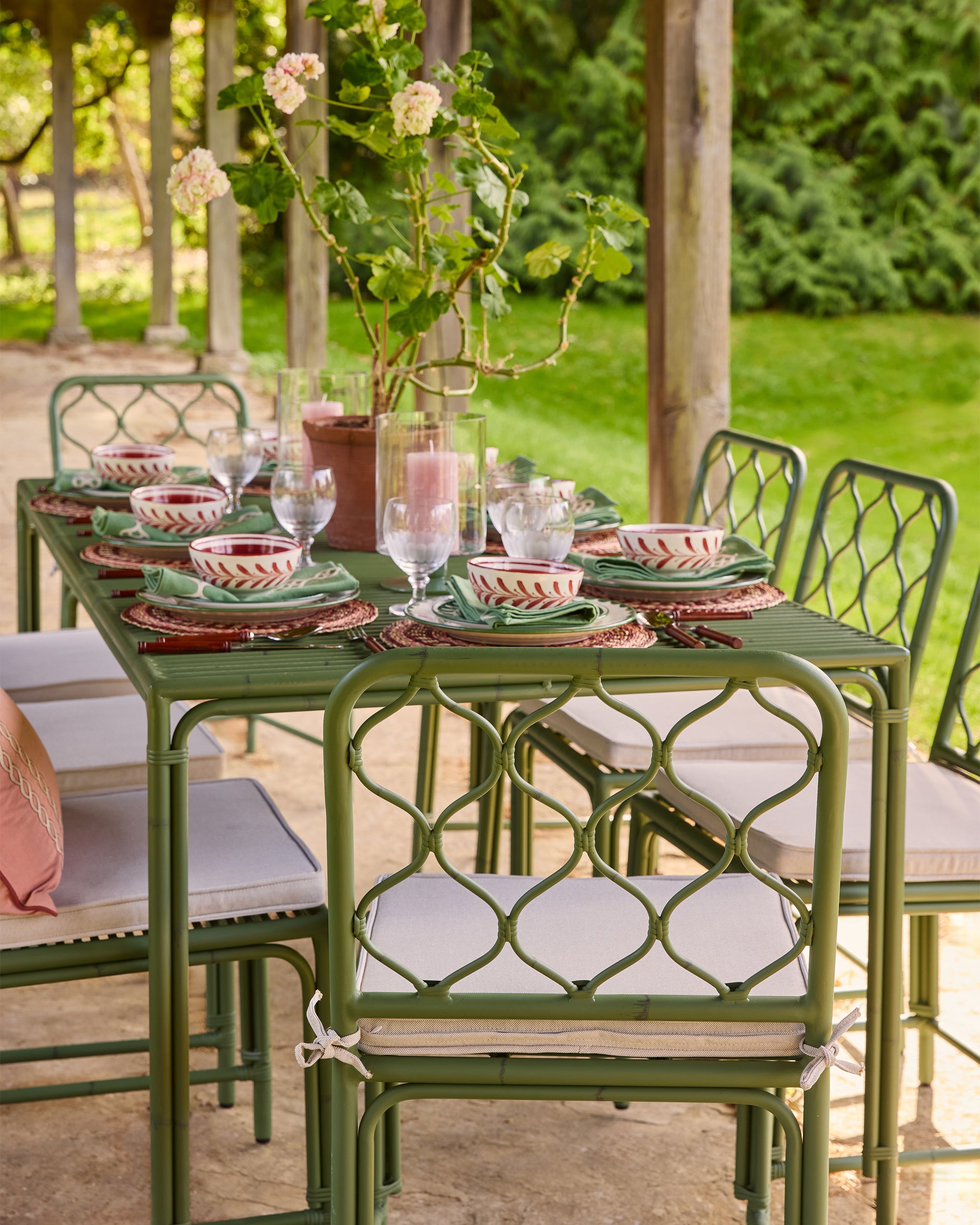 Outdoor dining table set with green chairs and pink tableware on a patio.