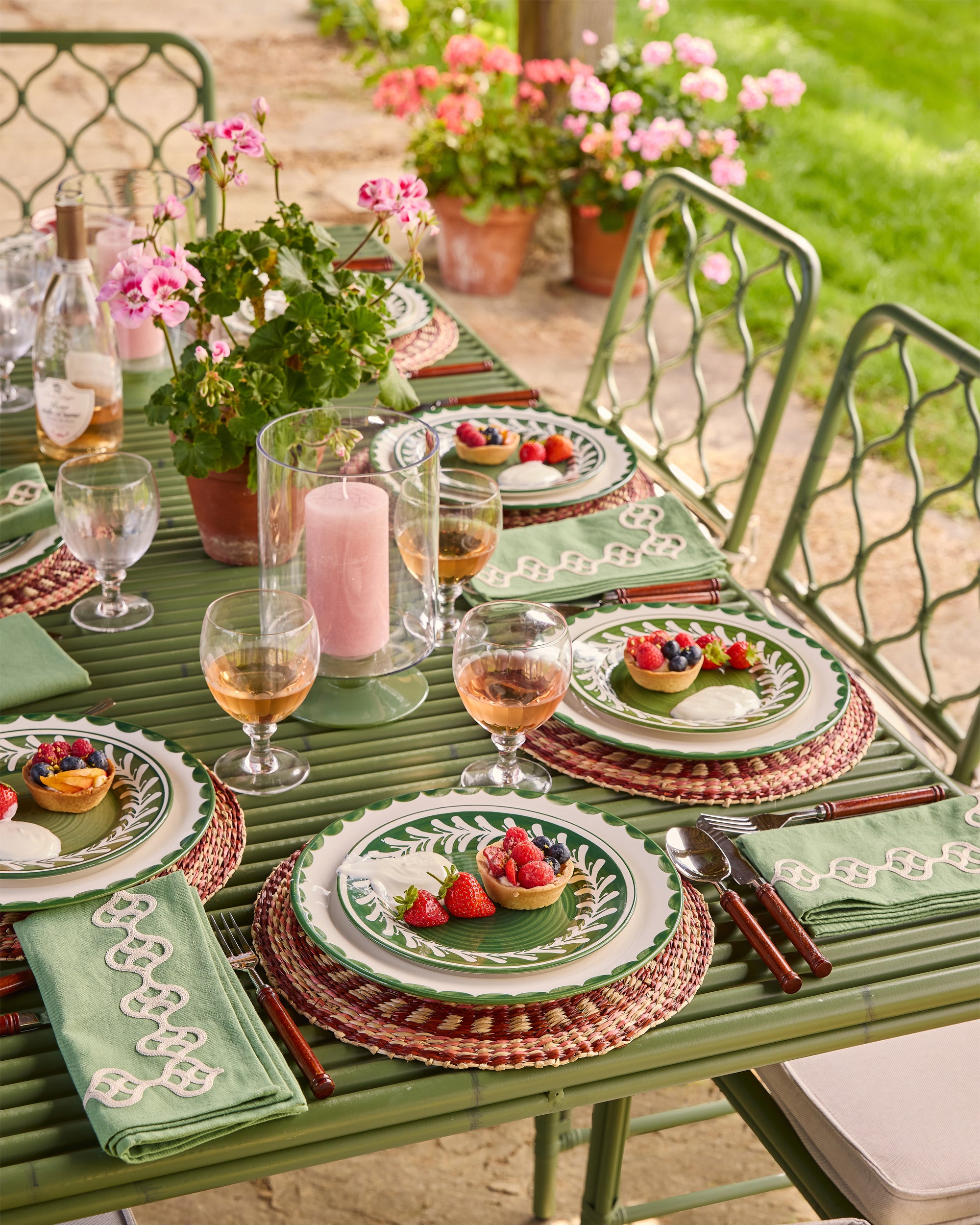 Outdoor dining table set with plates, glasses, and flowers on a patio.