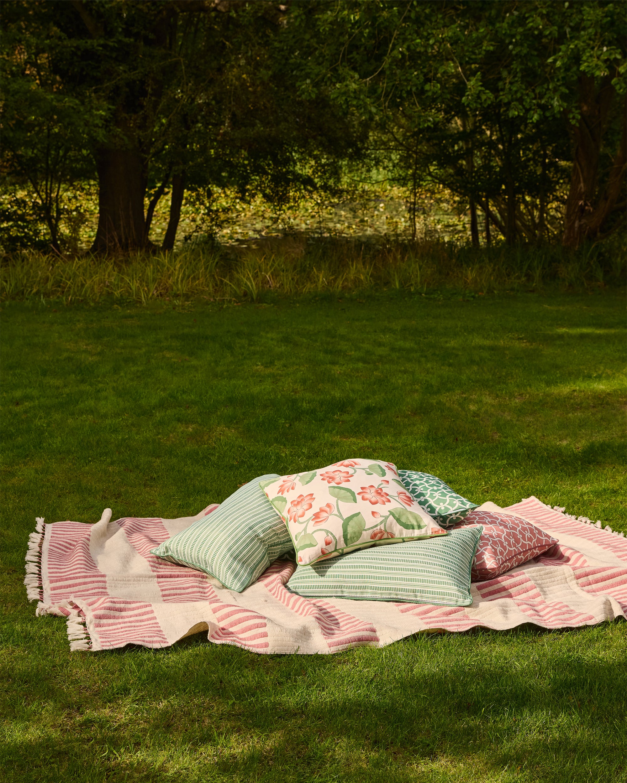 Pink and green patterned blanket with pillows on a grassy field