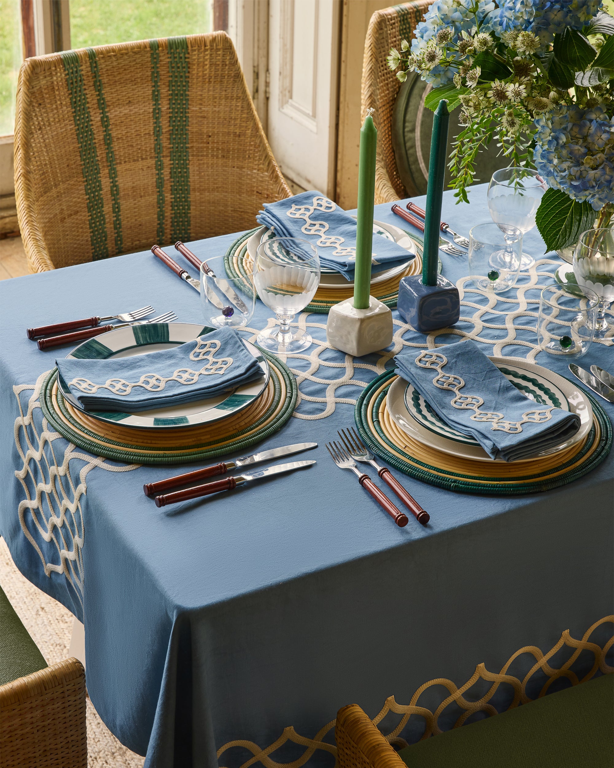 Elegant table setting with blue tablecloth, green candles, and decorative plates.