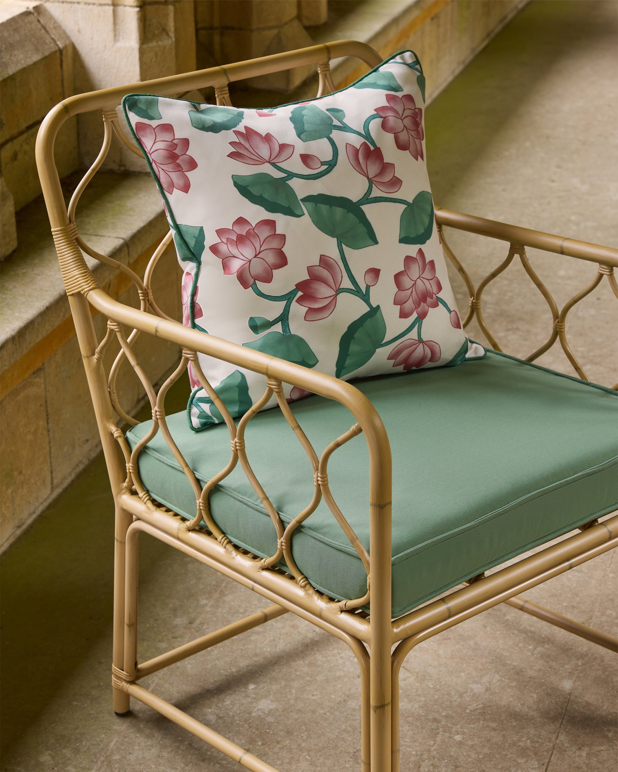 Rattan chair with a floral pillow and green cushion on a wooden floor.