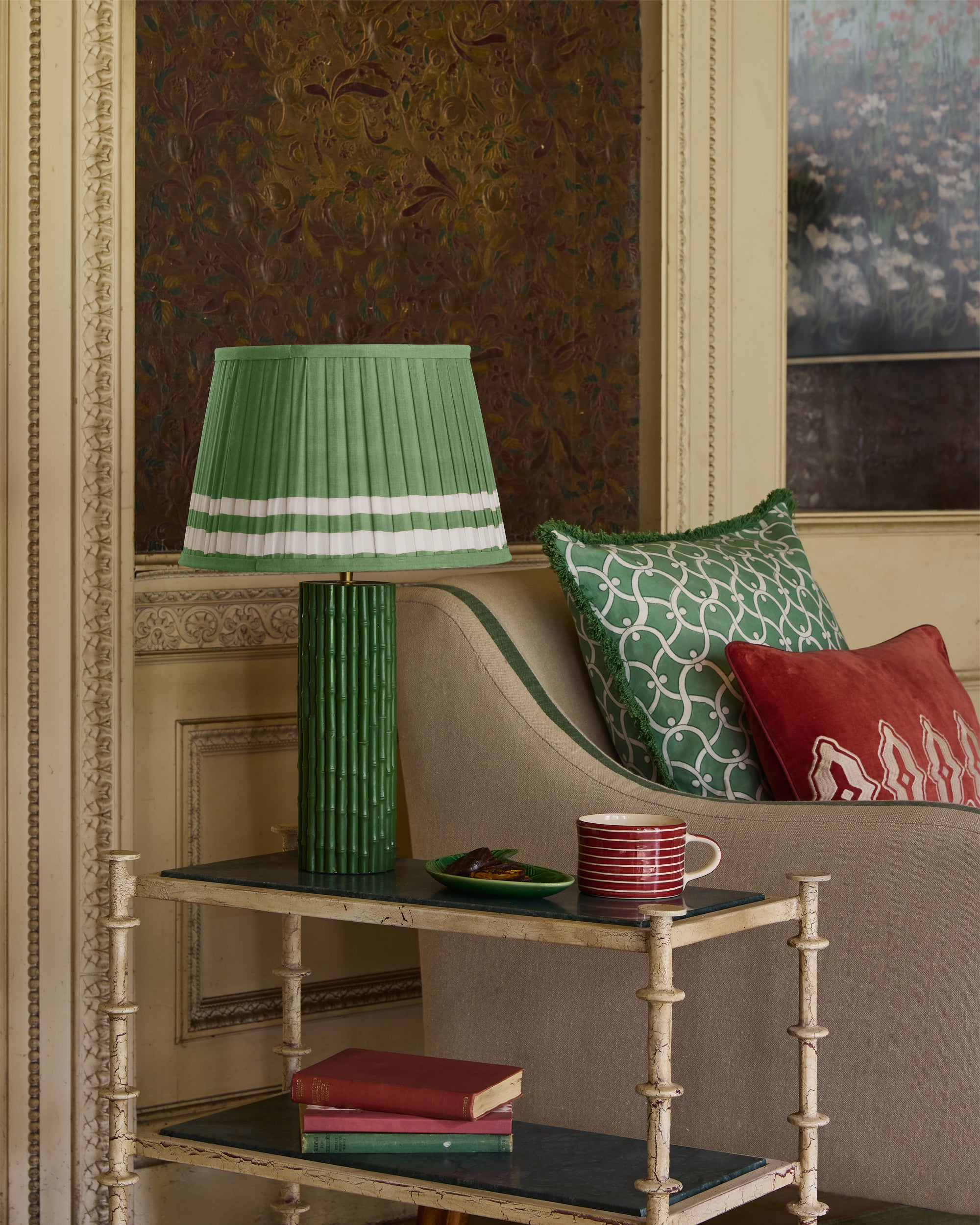 Decorative table with a green lamp, books, and cups against an ornate wall.