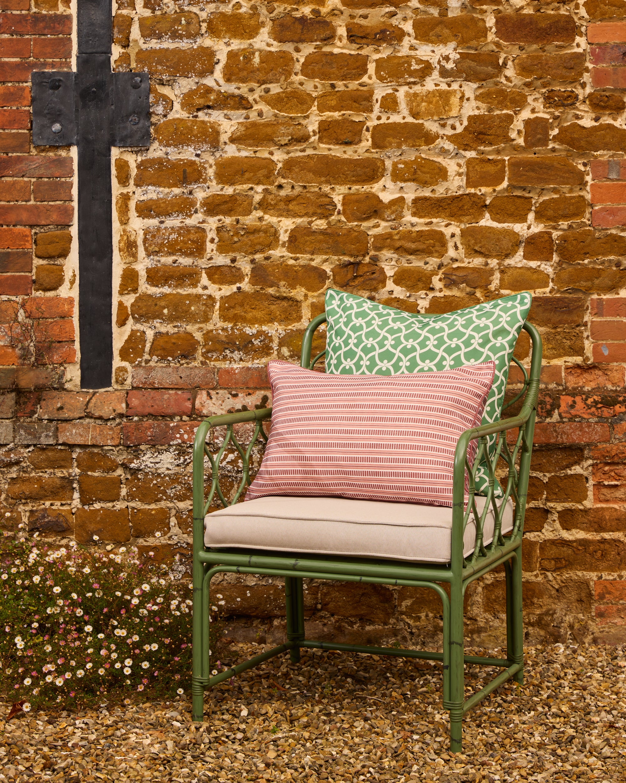 Green metal chair with cushions against a brick wall