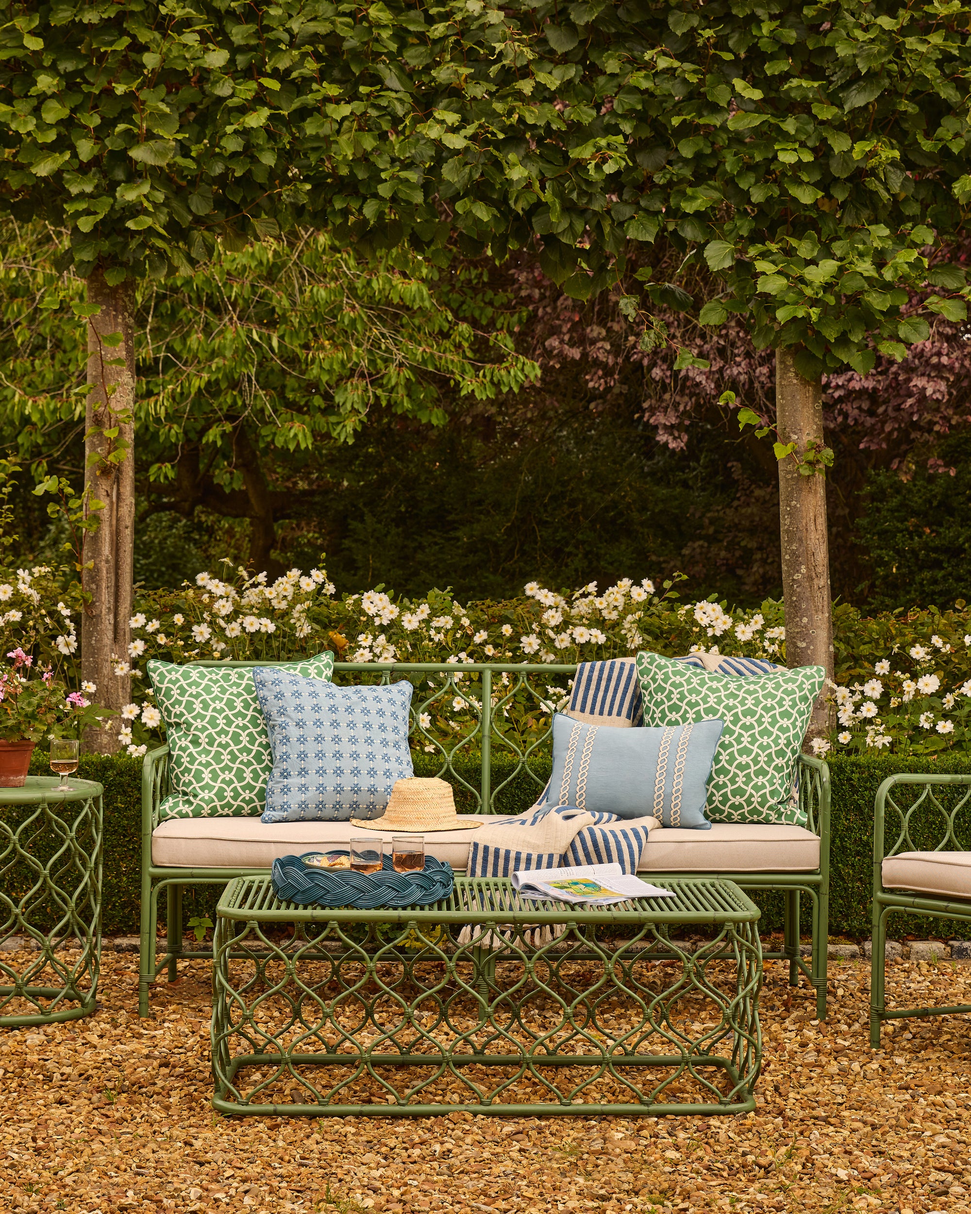 Outdoor garden setting with a green metal sofa and table, surrounded by flowers and greenery.