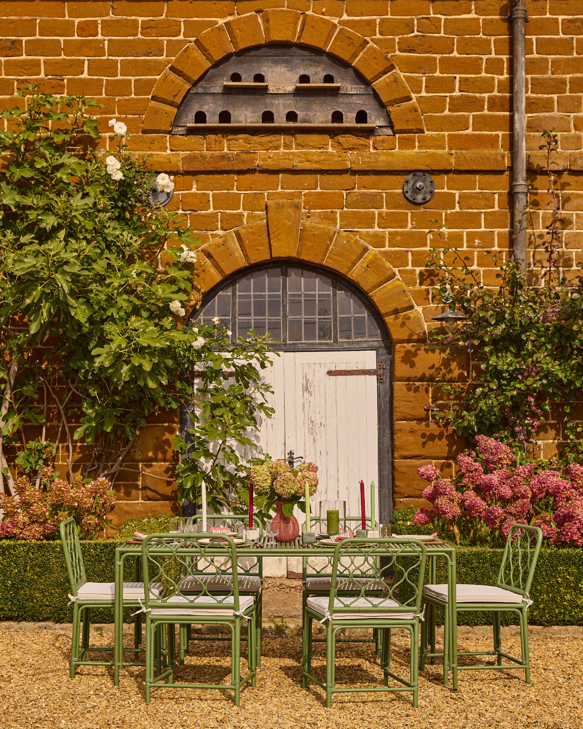 Outdoor setting with a table and chairs in front of a brick building with a white door.