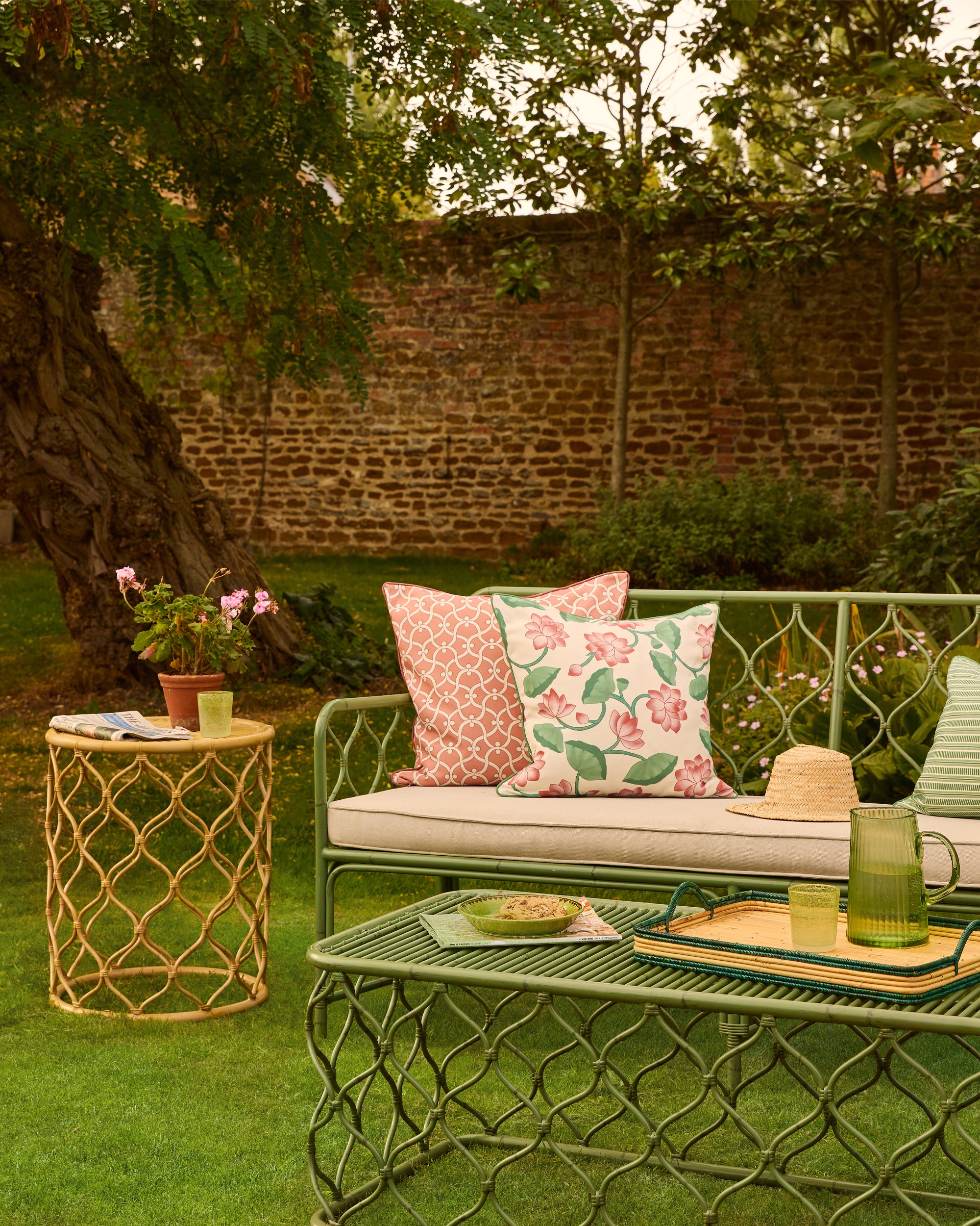 Outdoor garden setting with a green metal sofa, table, and decorative pillows.