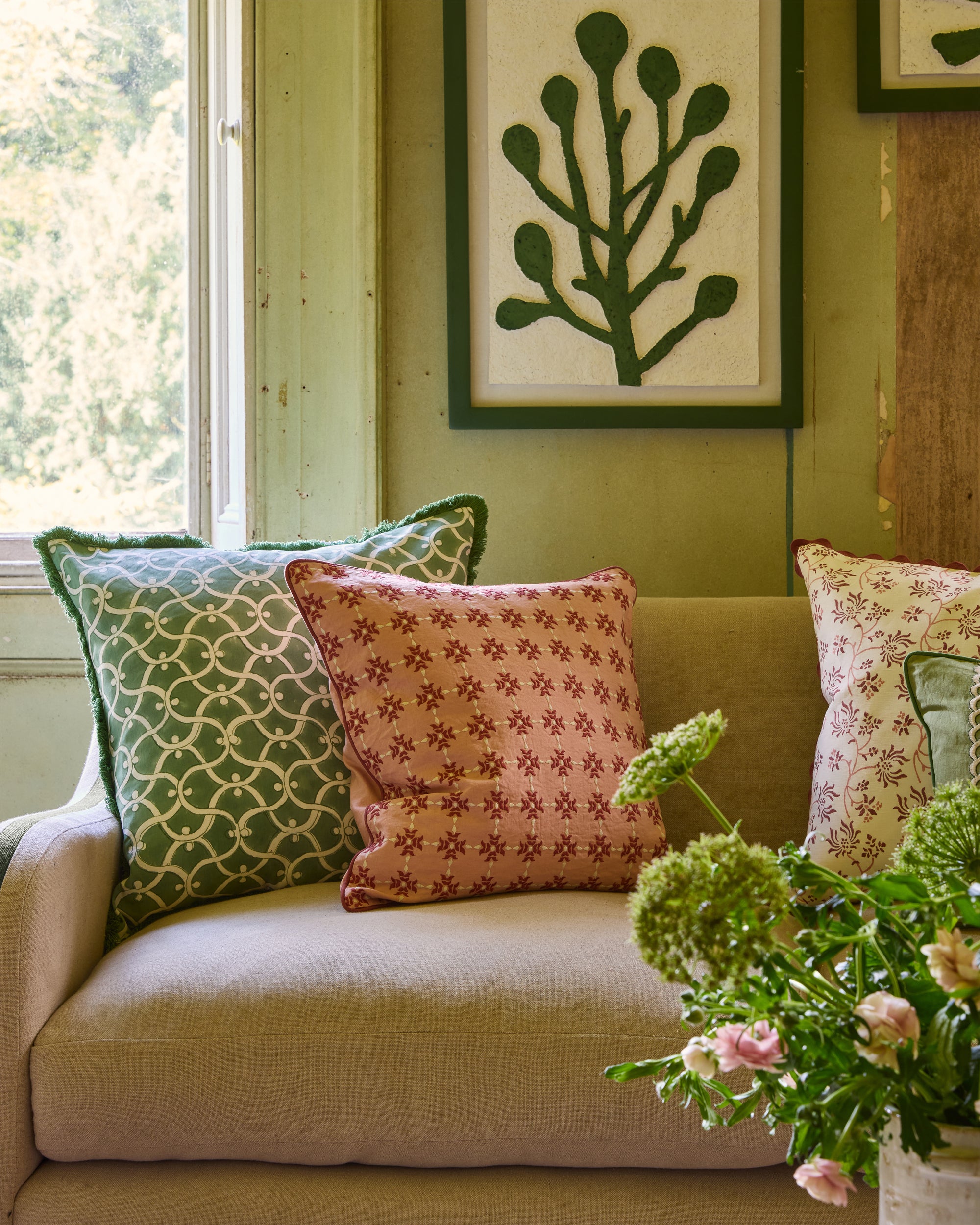 Decorative pillows on a beige sofa with a green wall and framed artwork.